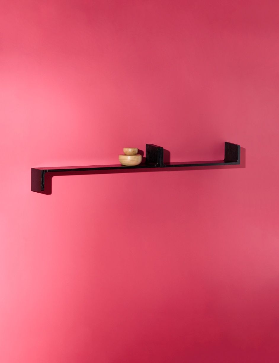 Schwarzes Ulna Wandregal von Schönbuch an pinker Wand mit zwei kleinen Holzschalen dekoriert.