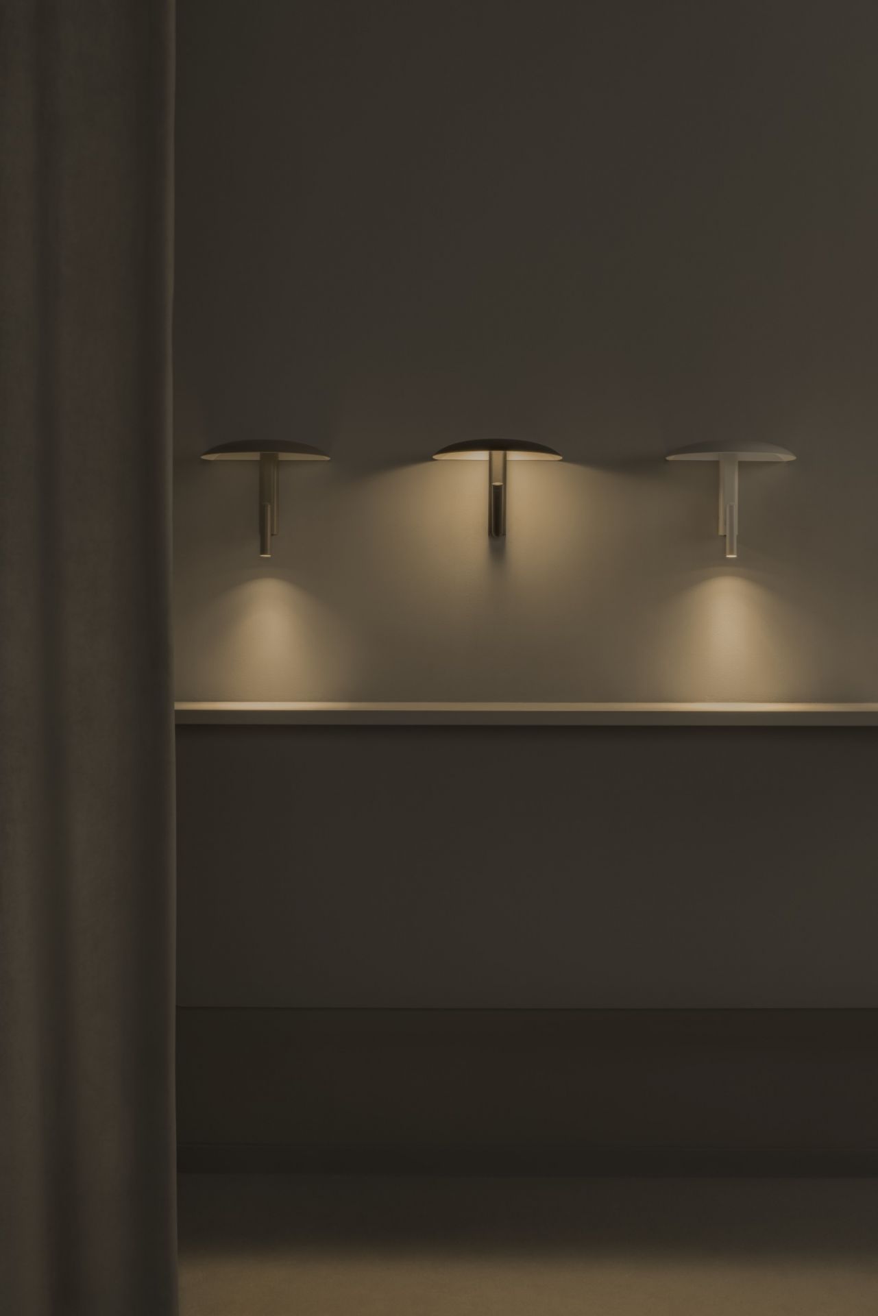 Drei Konoha Wandleuchten von Marset in verschiedenen Farben an einer Wand mit Vorhang.