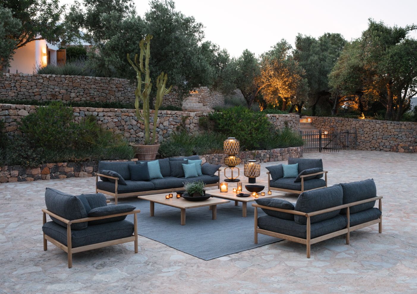 The Others Statue KAFA Leuchte Dedon Gartenmöbel-Set mit Sofa, Sesseln, Tisch und stimmungsvoller Beleuchtung im Außenbereich.