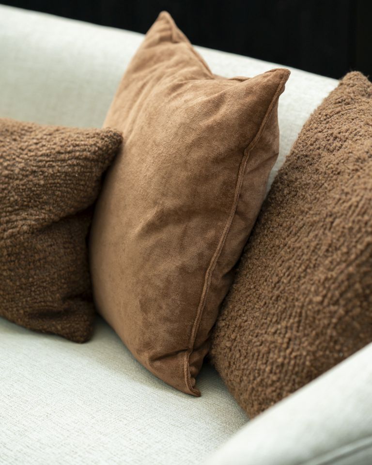 Nahaufnahme von drei braunen Zierkissen, darunter ein Ethnicraft Forest Samtkissen 50x50, auf einem hellen Sofa.