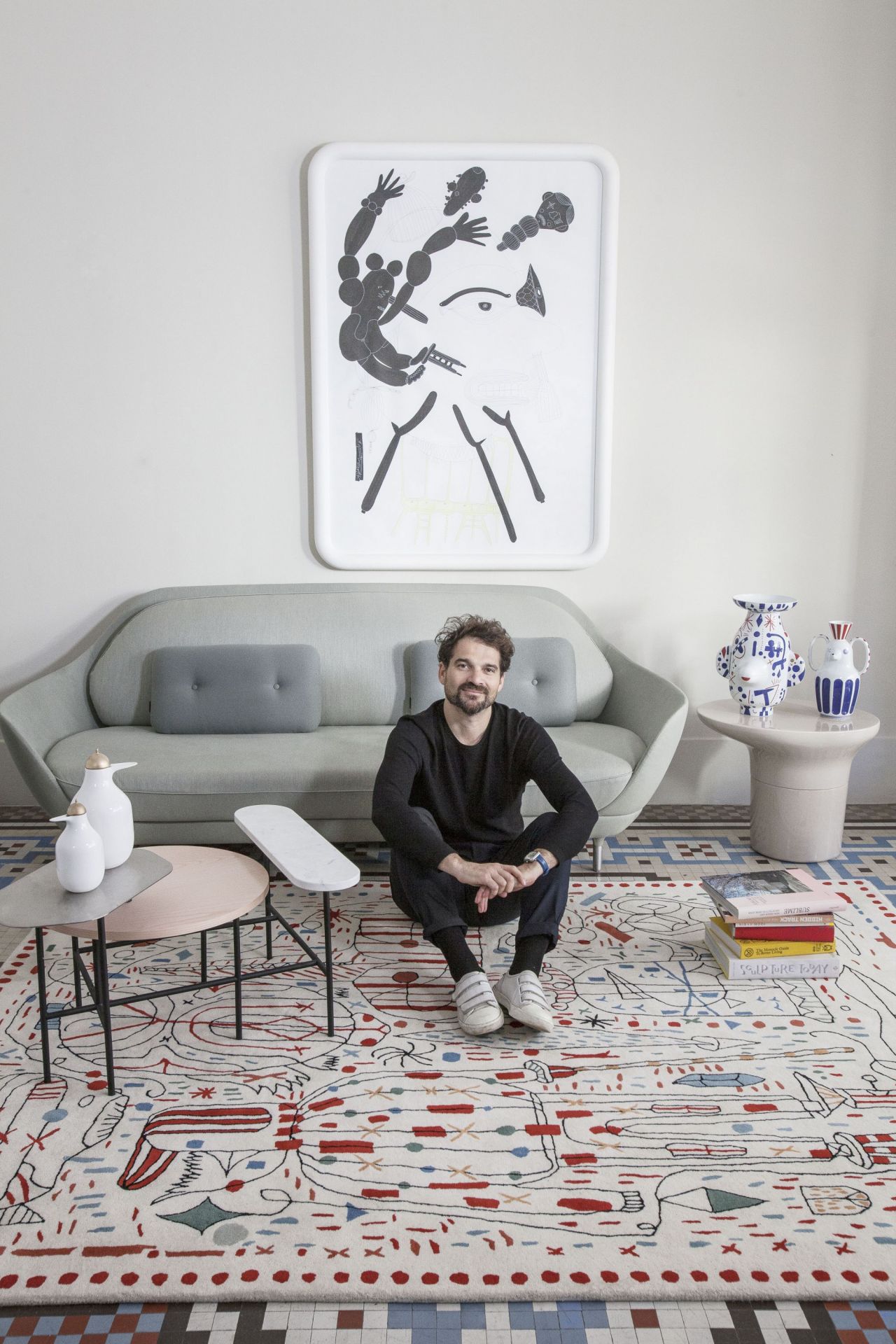Mann sitzt auf dem Hayon x Nani Teppich von Nanimarquina mit abstraktem Muster in Wohnraum.