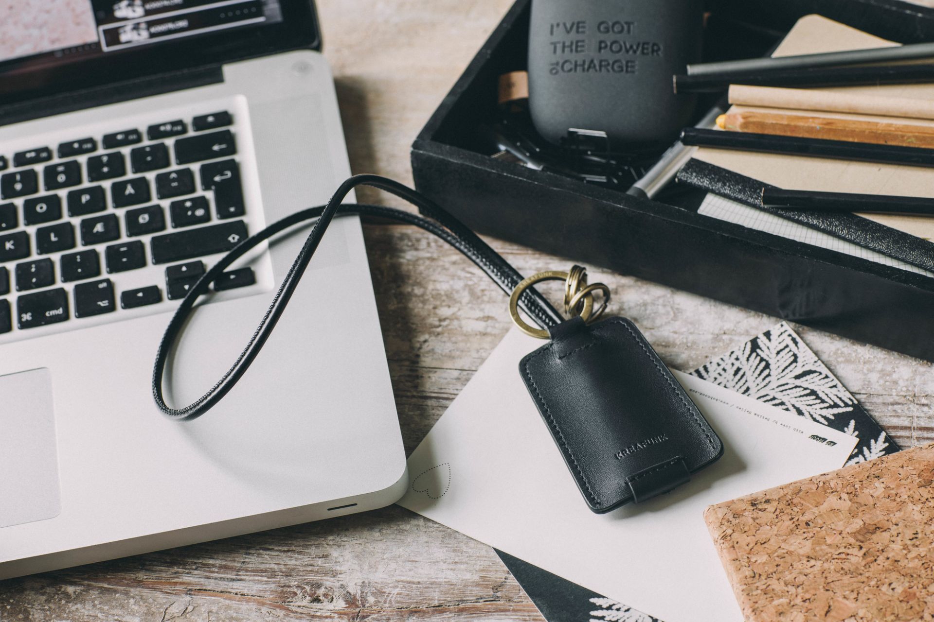 Schwarzer cCHAIN Schlüsselanhänger von Kreafunk mit USB-Kabel neben Laptop auf einem Schreibtisch.