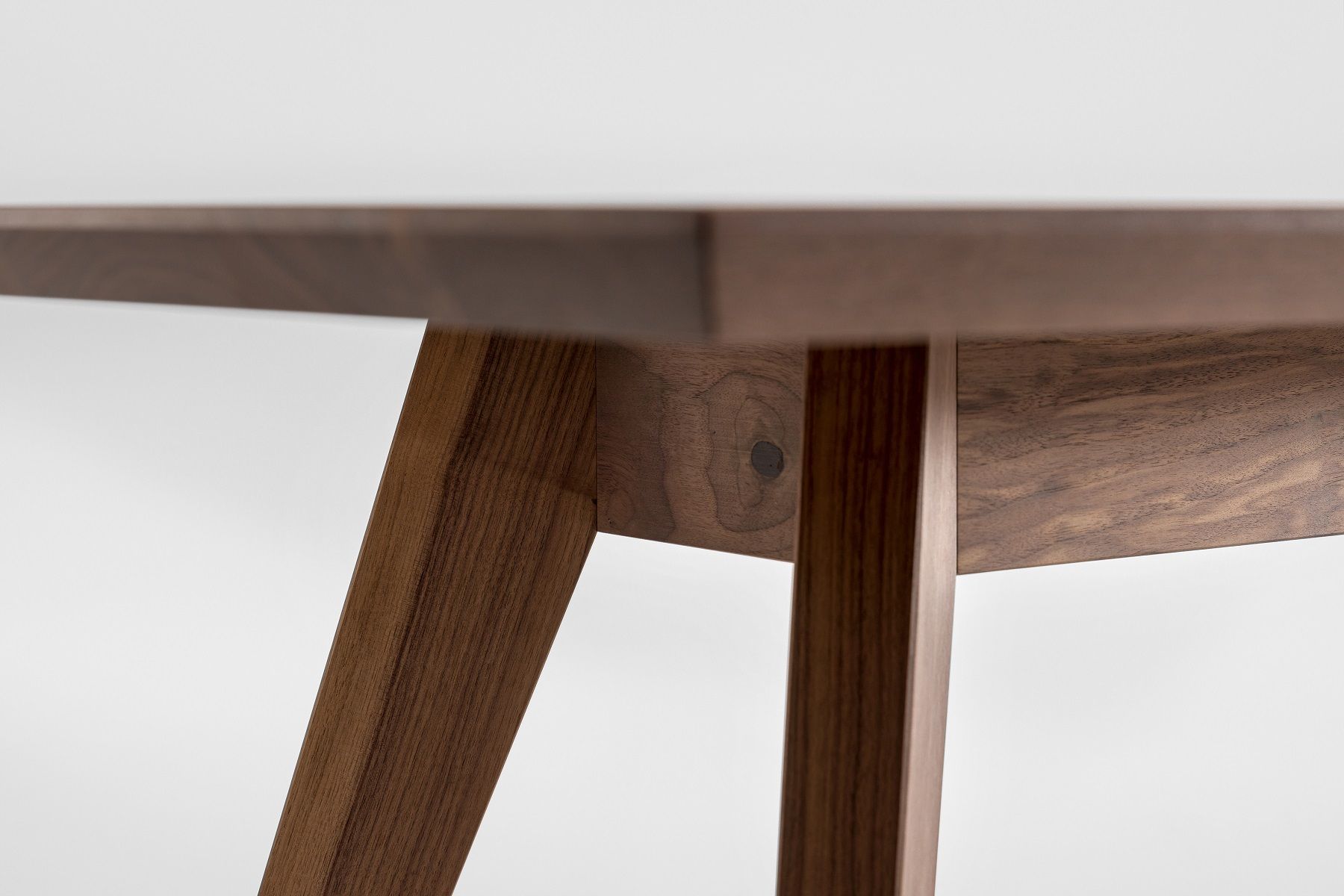 Detailansicht des CENA Tisches: Rechteckiger Esstisch aus dunklem Holz mit schrägen Beinen.