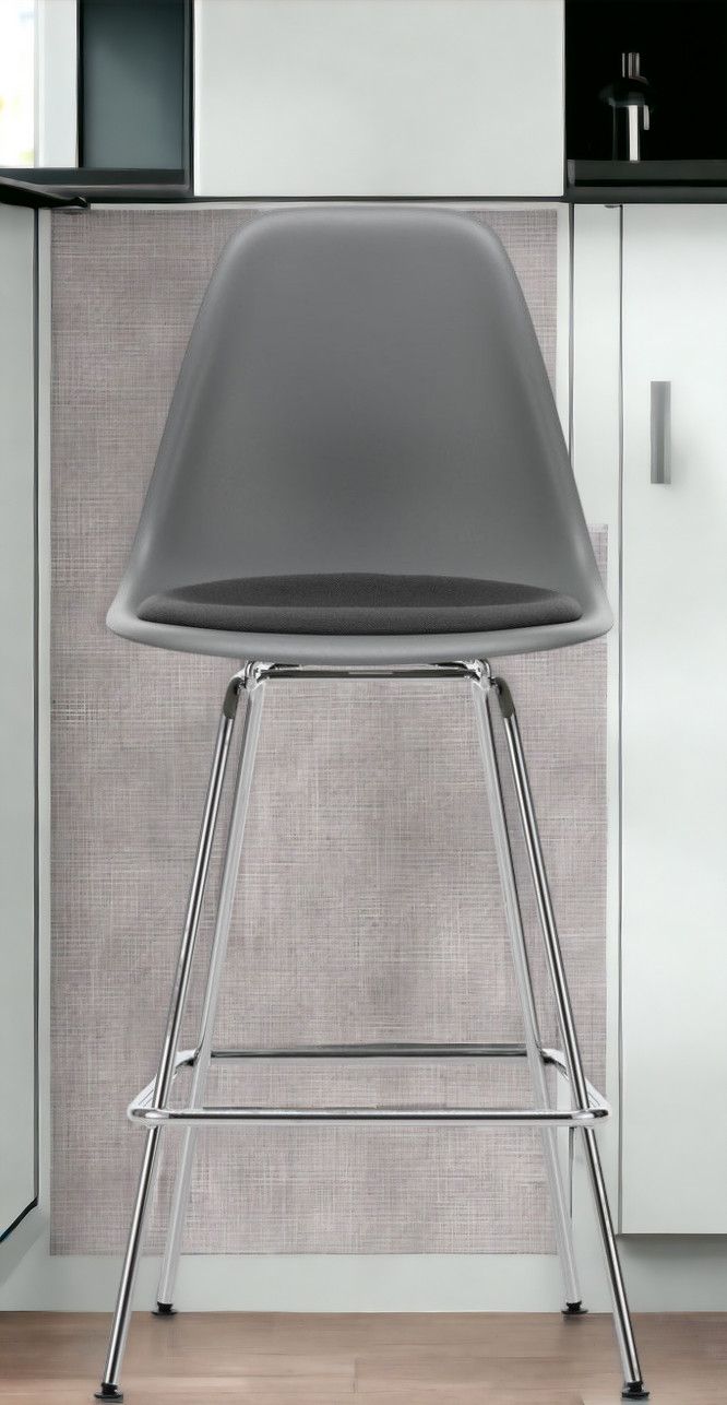 Grauer Eames Barhocker mit Sitzpolster und verchromtem Gestell vor Küchenzeile. Vitra Barstuhl.