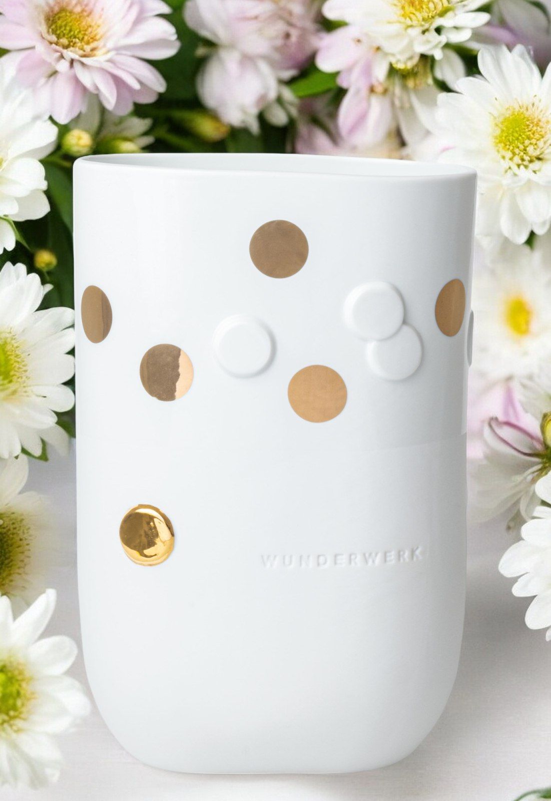 Weiße Vase "Wunderwerk" mit goldenen Punkten und Blumen im Hintergrund, dekorative Keramik für Zuhause.