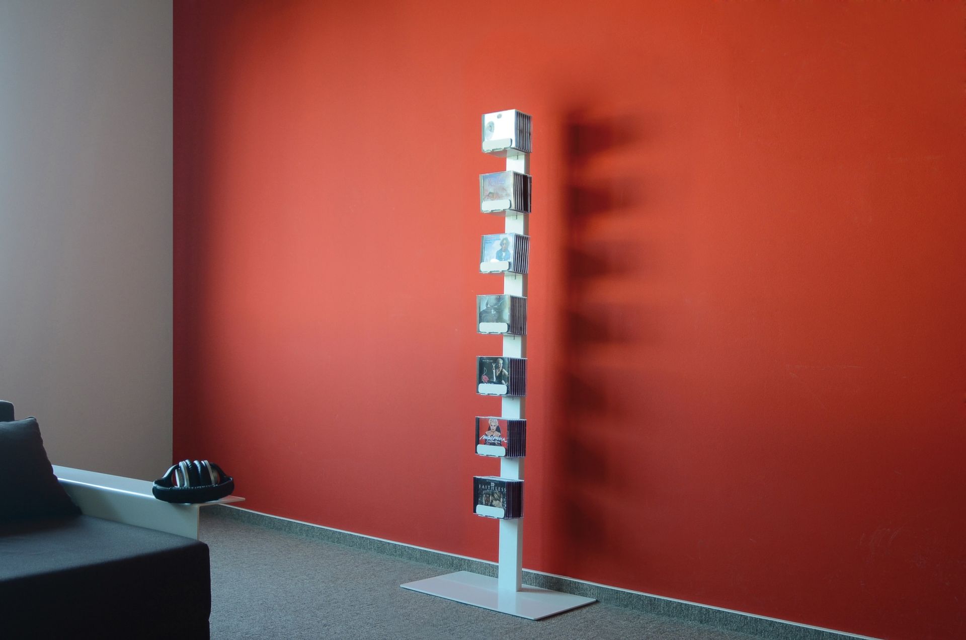 Weißes CD-Regal "CD-Baum" mit CDs vor roter Wand. Einzeln stehendes Standregal für CDs.