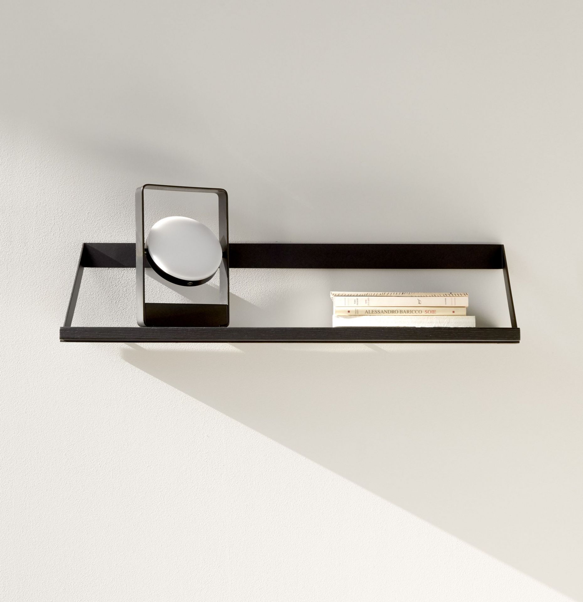 Ethnicraft Ribbon Regal aus schwarzem Eichenholz mit Lampe und Büchern an weißer Wand.