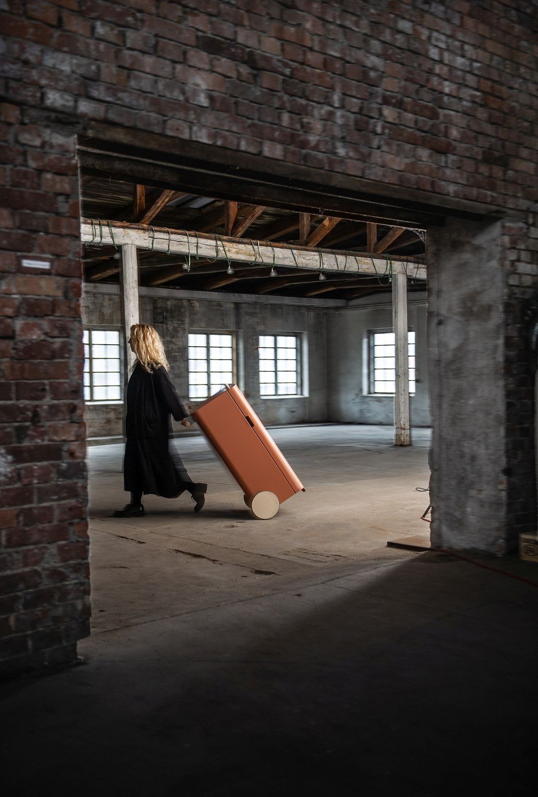 Frau zieht orangefarbenen Arkityp Mülleimer/Mülltrennung mit Rollen durch einen Raum.