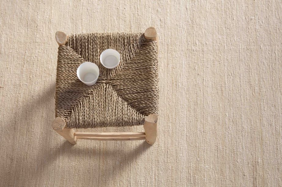 Detailaufnahme: Grauer Nomad Teppich von Nanimarquina mit Stuhl und zwei Tassen. Hochwertiger Teppich für Wohnräume.