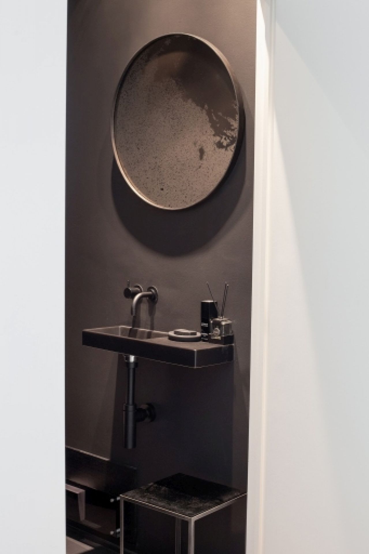 Runder Wandspiegel "heavy aged bronze" von Ethnicraft über einem dunklen Waschbecken in einem modernen Badezimmer.