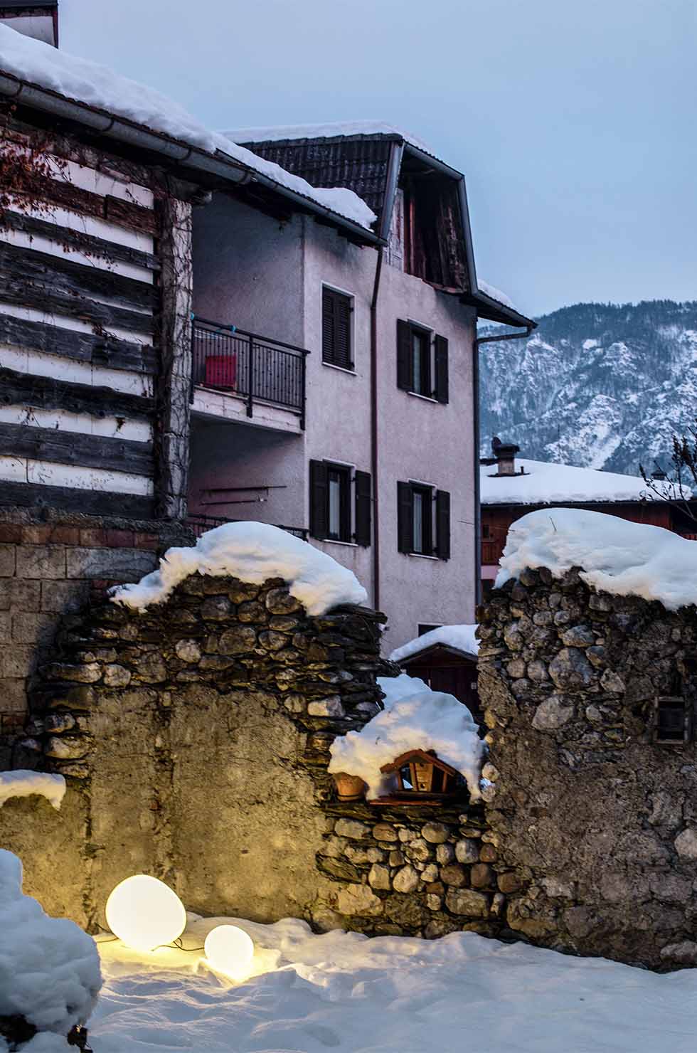 Zwei Gregg Outdoor Leuchten von Foscarini im Schnee vor einem alten Haus.