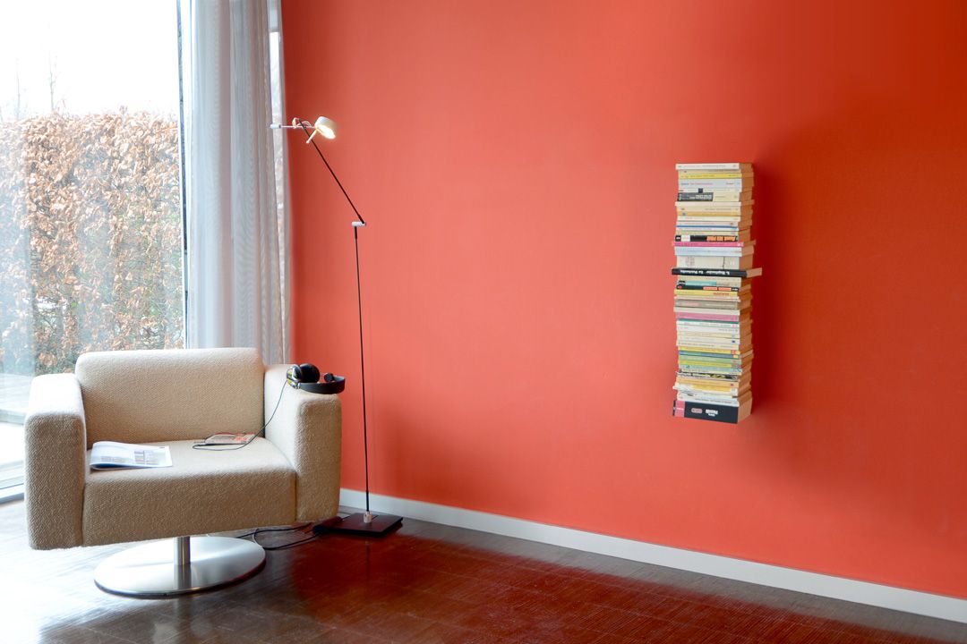 Booksbaum Wandregal mit Büchern an roter Wand, neben Sessel und Stehlampe.