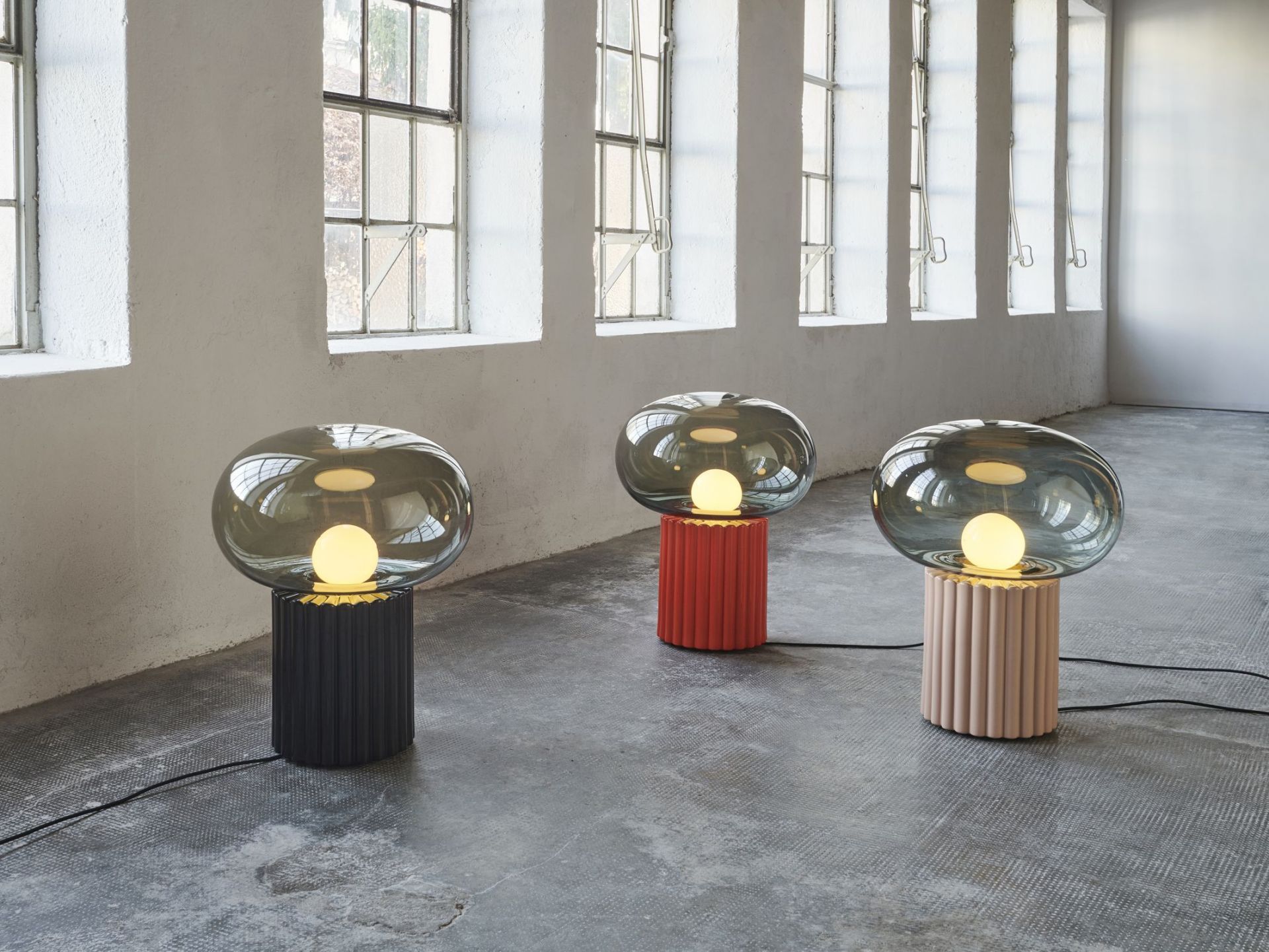 Drei Fungi Bodenleuchten mit farbigen, geriffelten Sockeln und runden, rauchglasfarbenen Lampenschirmen.