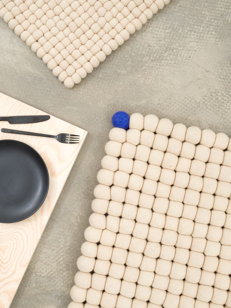 Beiger Filzteppich "Big One" von myfelt (140x200 cm) mit Filzkugeln und blauer Akzentkugel.