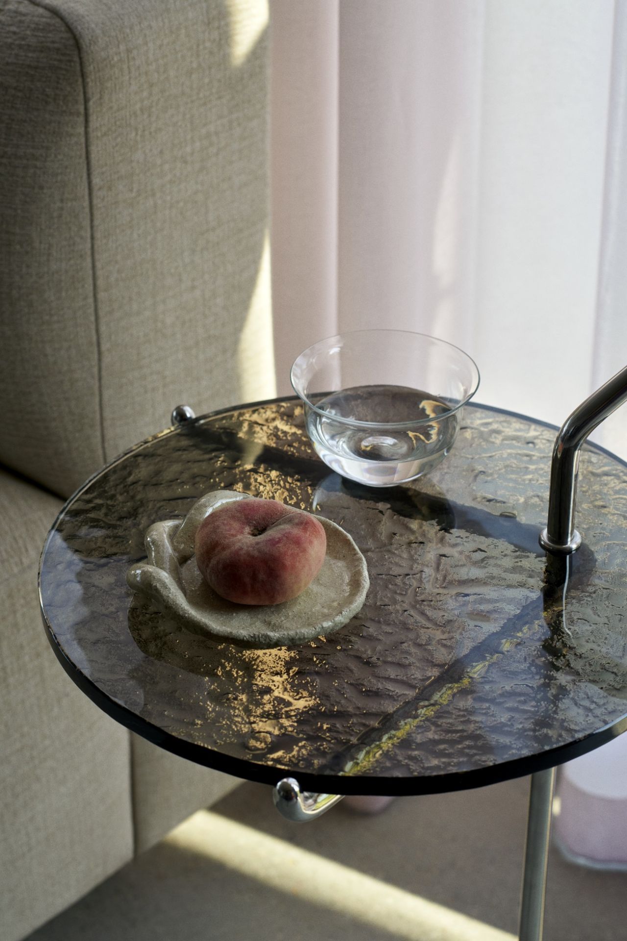 Nahaufnahme des AndTradition Halten SH9 Beistelltisches mit Pfirsich und Wasserglas. Moderner, runder Beistelltisch.