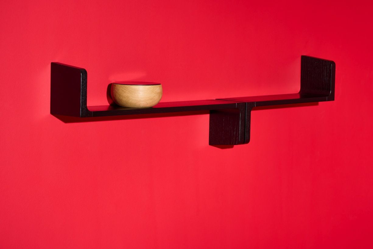 Schwarzes Ulna Wandregal von Schönbuch an roter Wand mit dekorativer Holzschale.