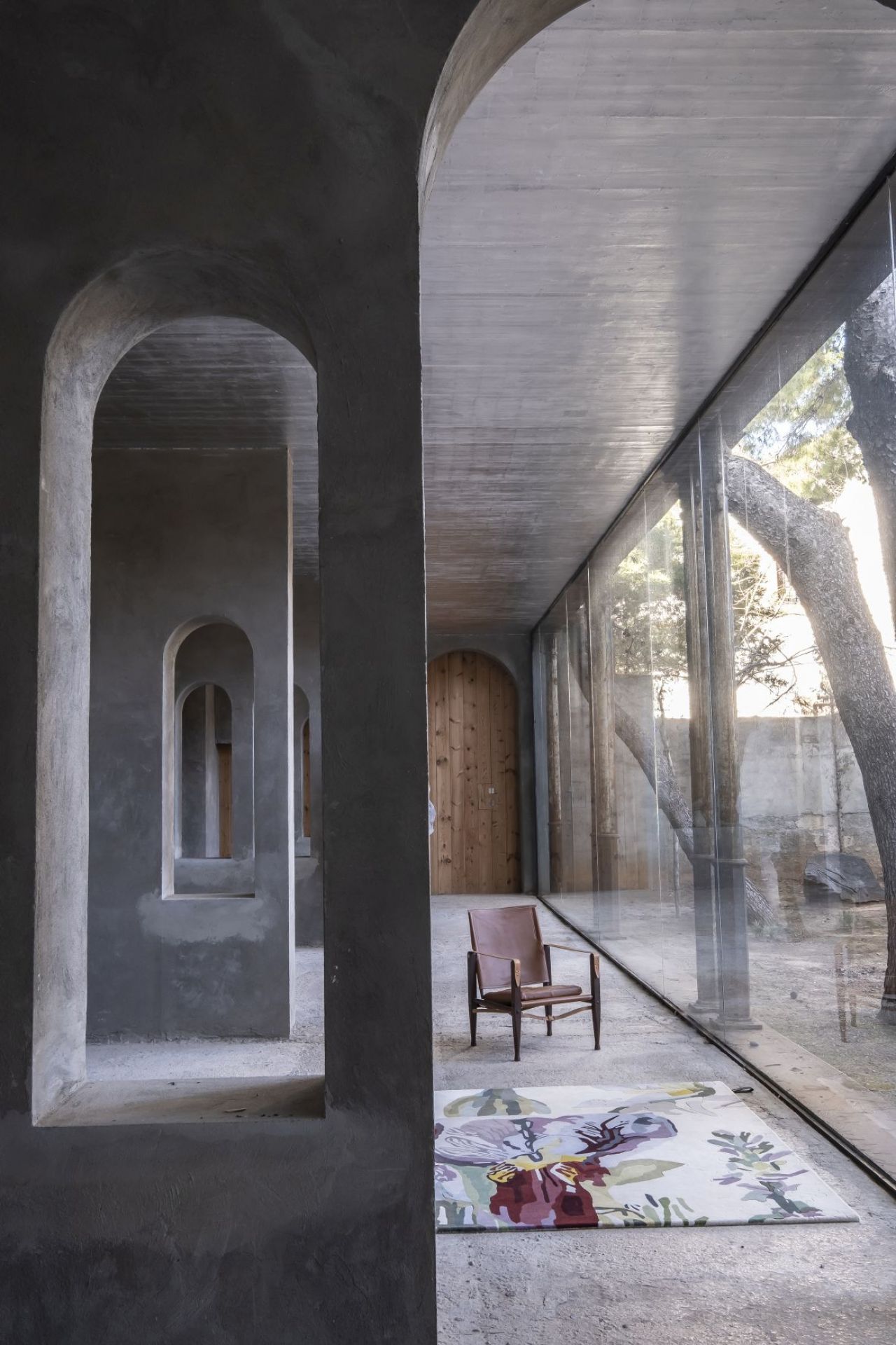 Innenaufnahme mit Nanimarquina Teppich "Flora Backyard", floralem Muster und braunem Sessel vor Fensterfront.