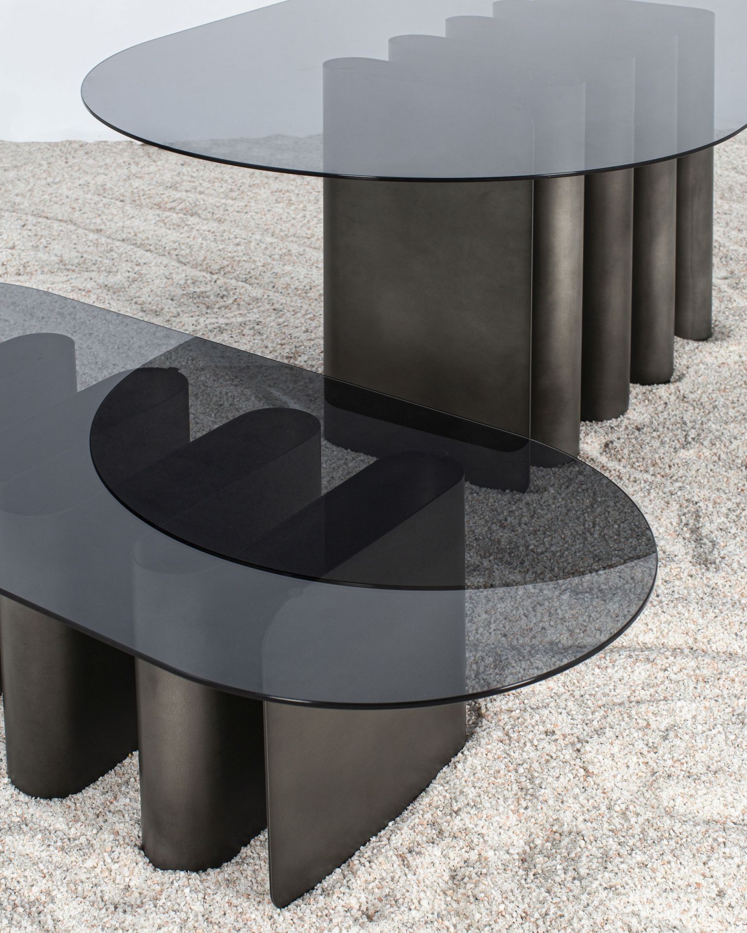 Tavolino2 Beistelltisch Pulpo mit grauer Glasplatte und zylinderförmigem Metallfuß auf hellem Teppich.