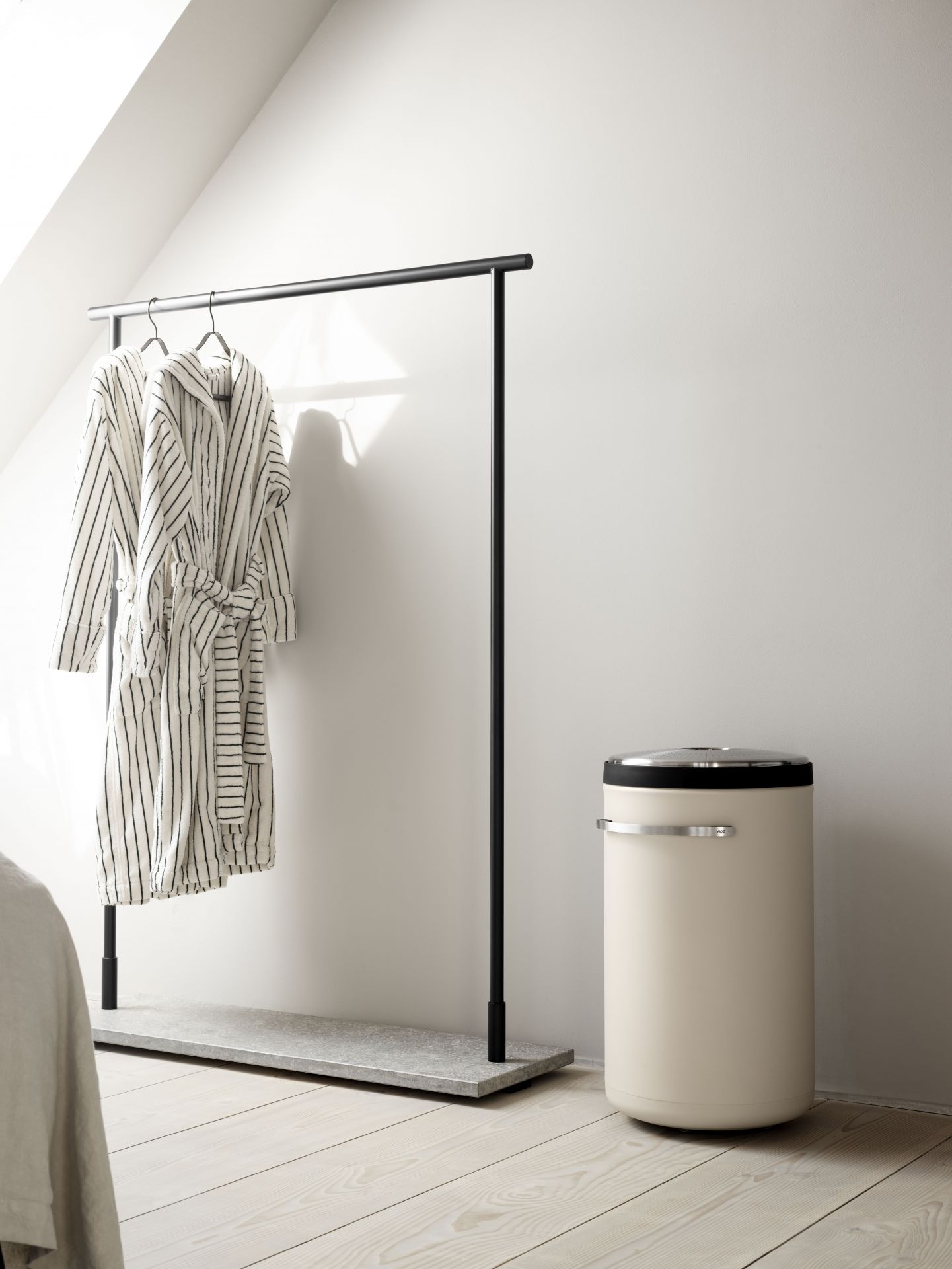 Beige Vipp Wäschekorb im minimalistischen Badezimmer neben Kleiderständer mit Bademänteln auf hellem Holzboden.