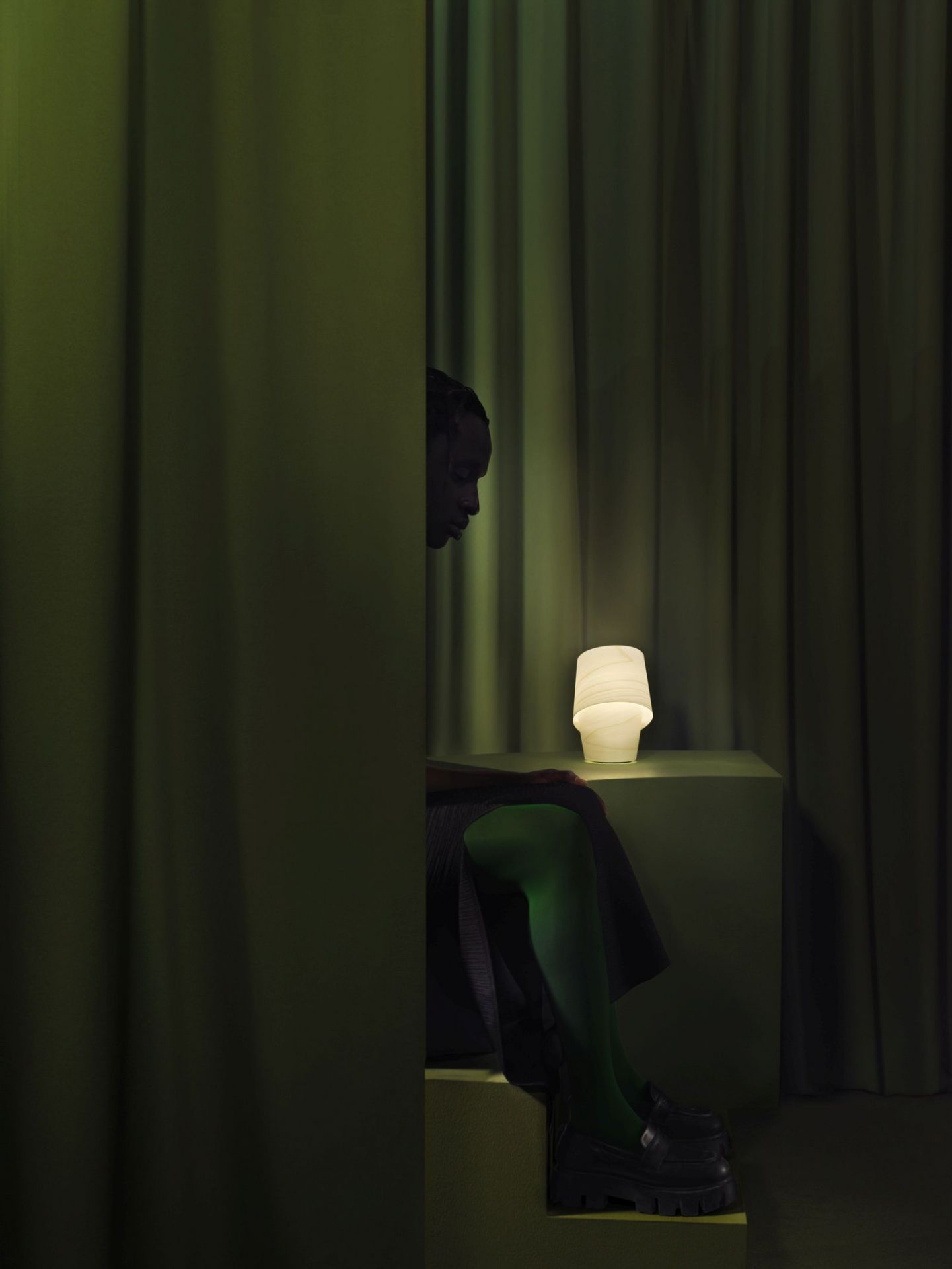 Nahaufnahme der LZF Lamps Tiny Tischleuchte mit warmem Licht, neben einer Person in grünen Strümpfen.