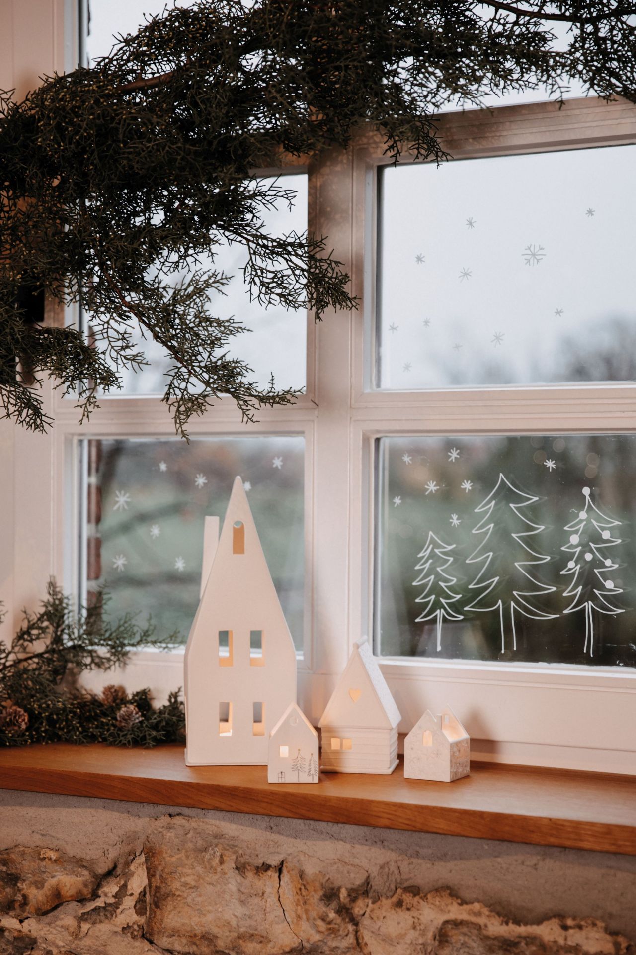 Weihnachtliche Dekoration mit Lichthaus Spitzdach, Keramik Häuser und Fensterbild mit Tannenbäumen.