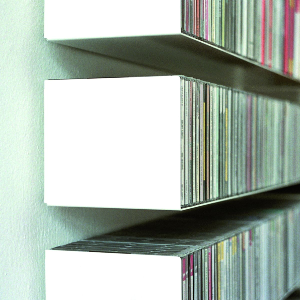 Weißes CD-Regal Linea1 von Müller Möbelwerkstätten, gefüllt mit CDs, an einer Wand befestigt.