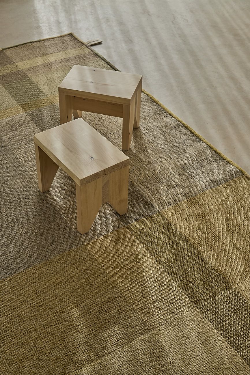 Nuance Teppich Nanimarquina: Detailaufnahme des Teppichs mit geometrischem Muster in Limettönen und zwei Holzhockern.