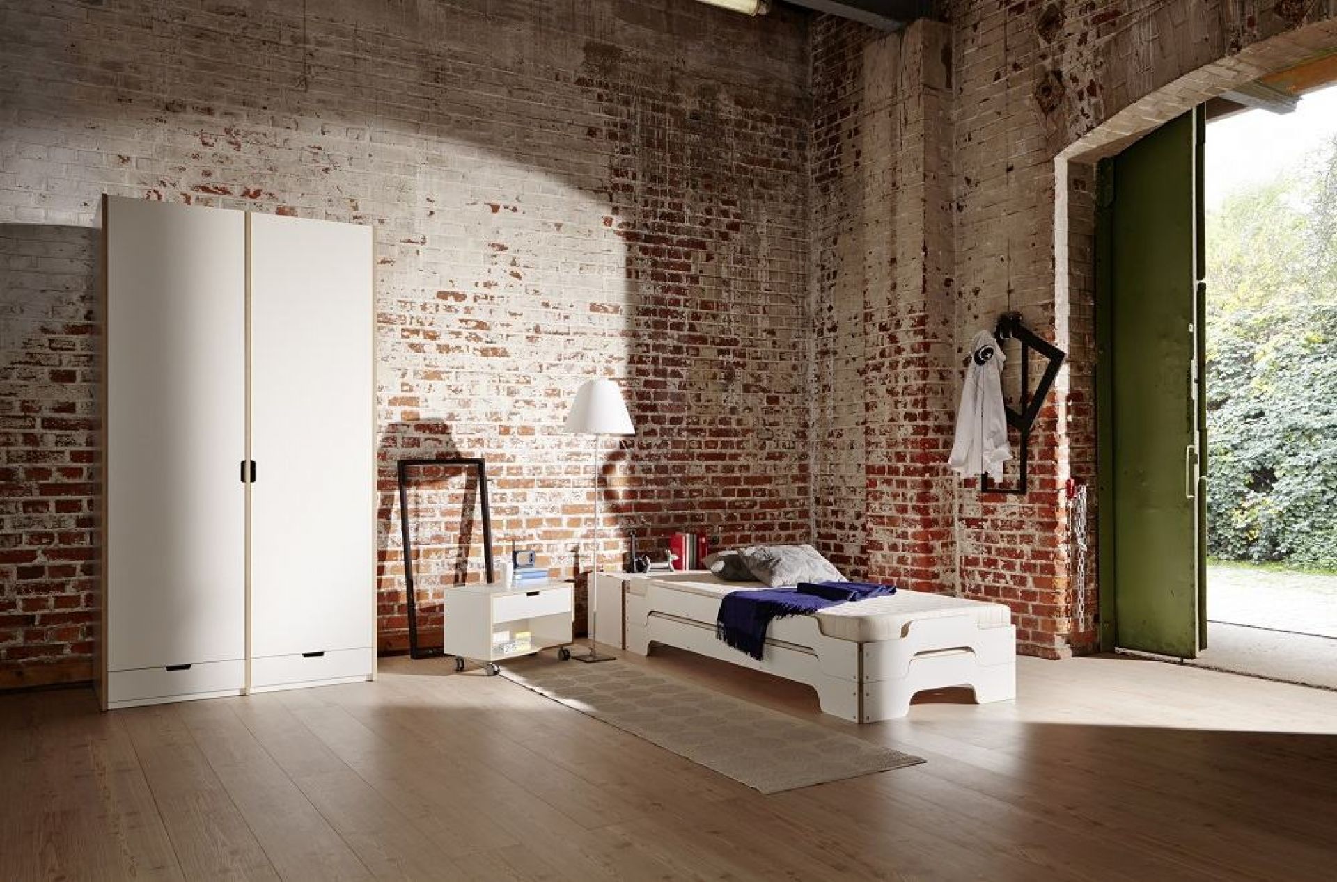 Weißer Modular Nachttisch von Müller Möbelwerkstätten neben Bett und Kleiderschrank in Loft-Atmosphäre.