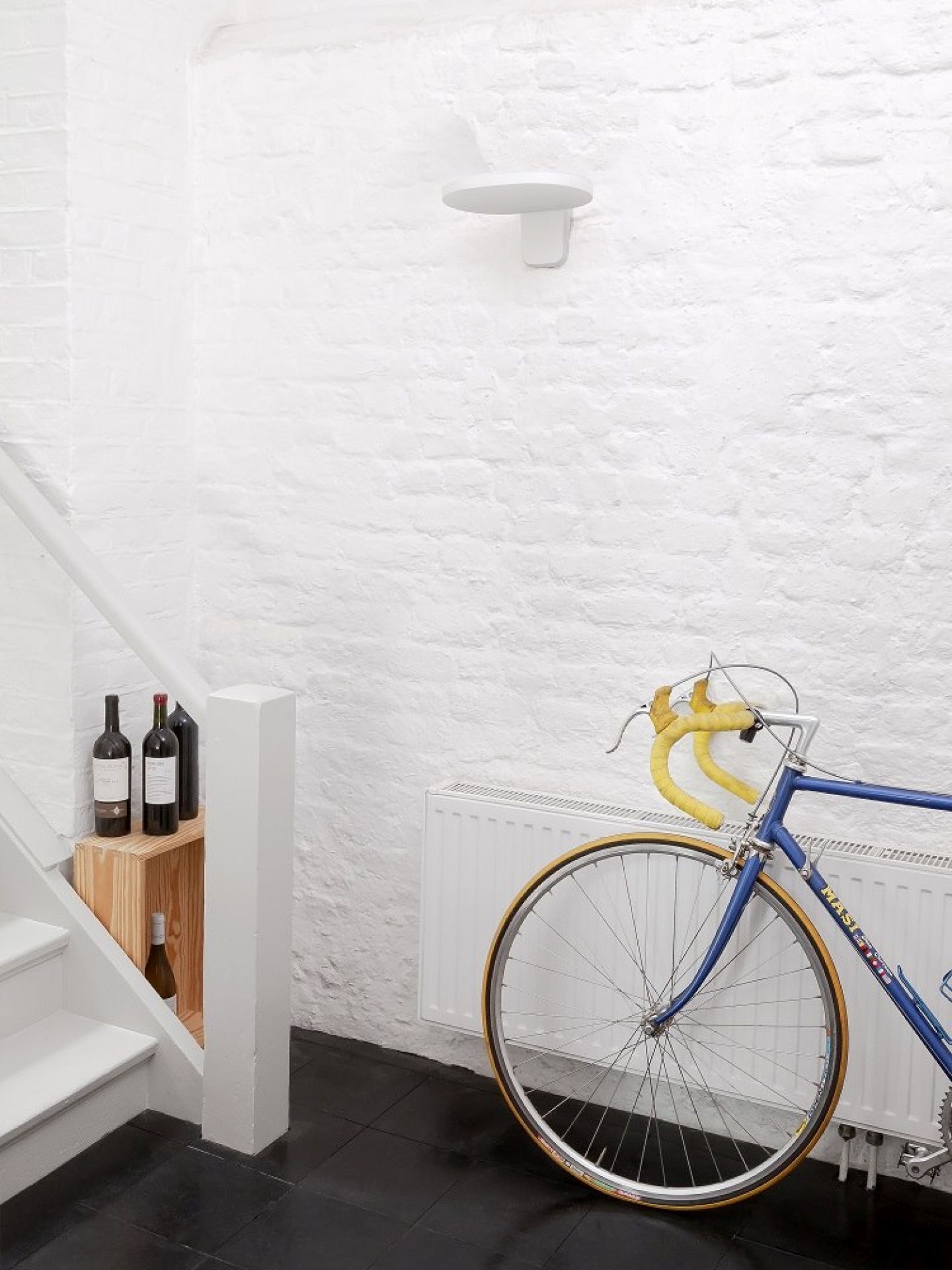 Helle Flos Wandleuchte Oplight W1 in Weiß an einer weißen Wand, kombiniert mit Fahrrad.