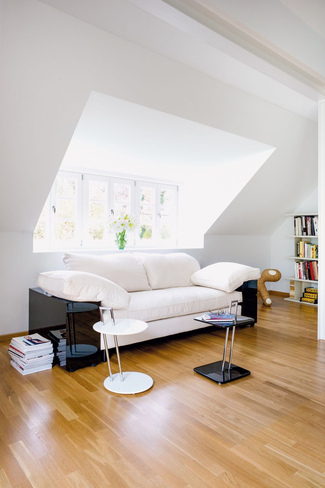 Helles Wohnzimmer mit Classicon Lota Sofa, Beistelltischen und Bücherregal unter einer Dachschräge.