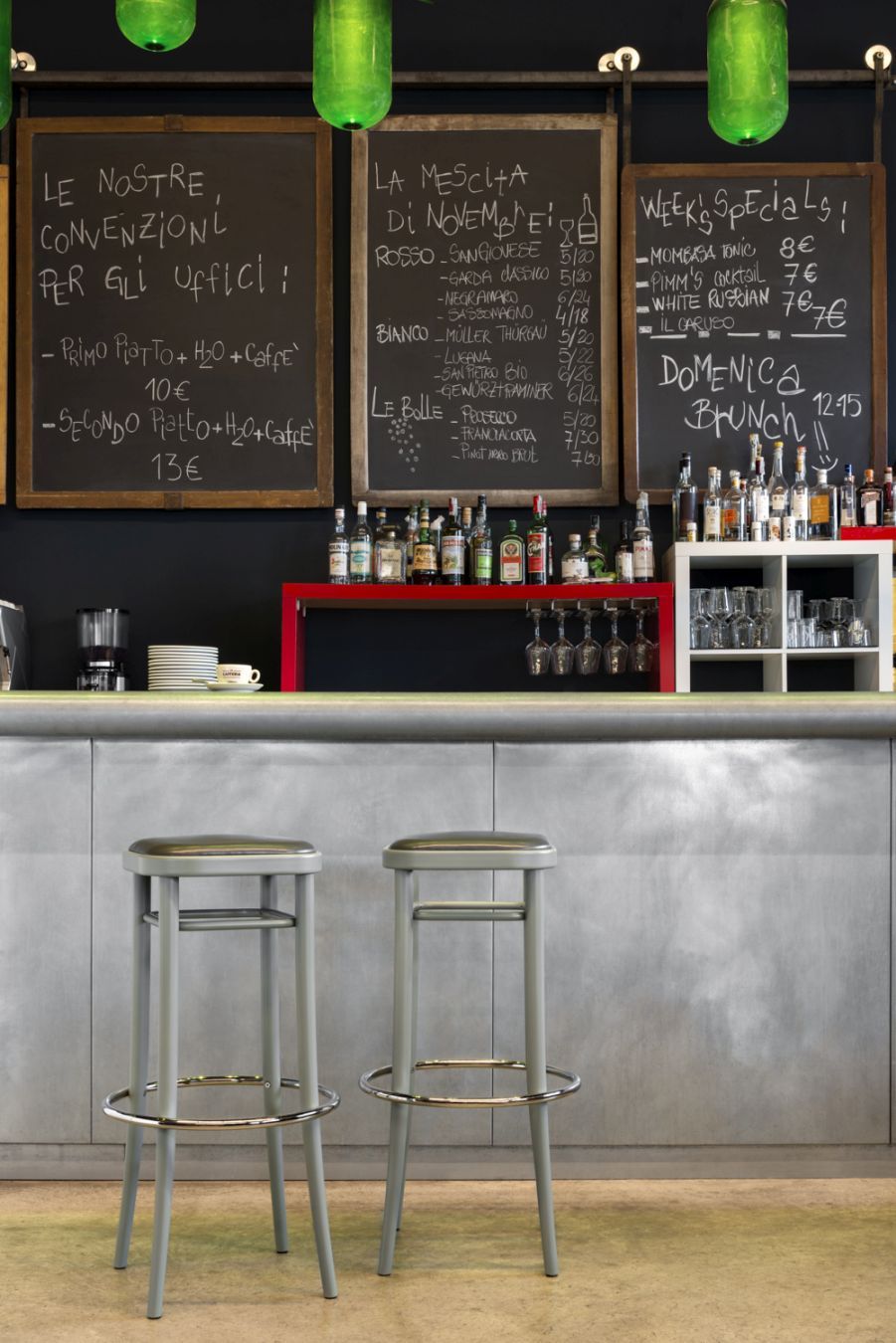 Zwei graue Vienna 144 Barhocker mit Schichtholzsitz vor einer Bar mit Getränken.