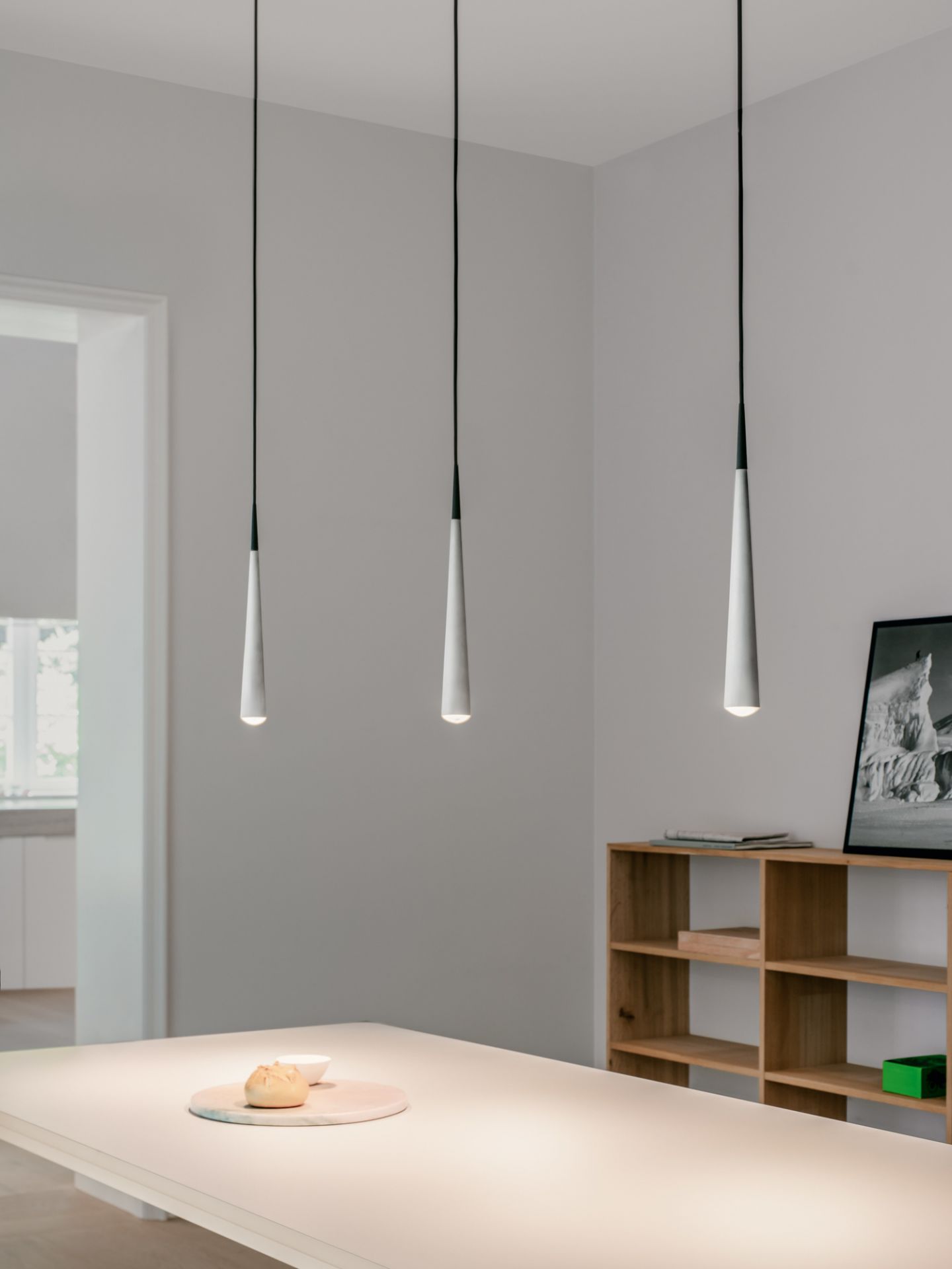 Drei graue Niceone Trace Pendelleuchten über einem Esstisch, moderne Innenraumbeleuchtung.