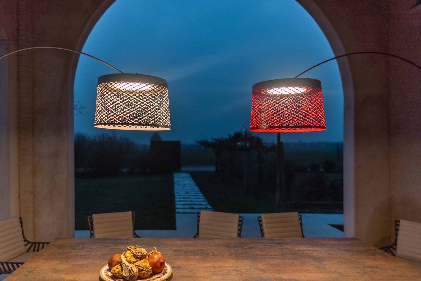 Zwei Twiggy Grid Stehleuchten von Foscarini, eine kaminrot, hängen über einem Esstisch im Freien.