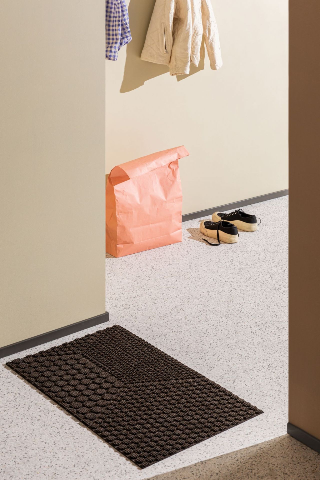 Braune Hex Fußmatte Soil von Heymat im Eingangsbereich mit Schuhen und Papiertüte.