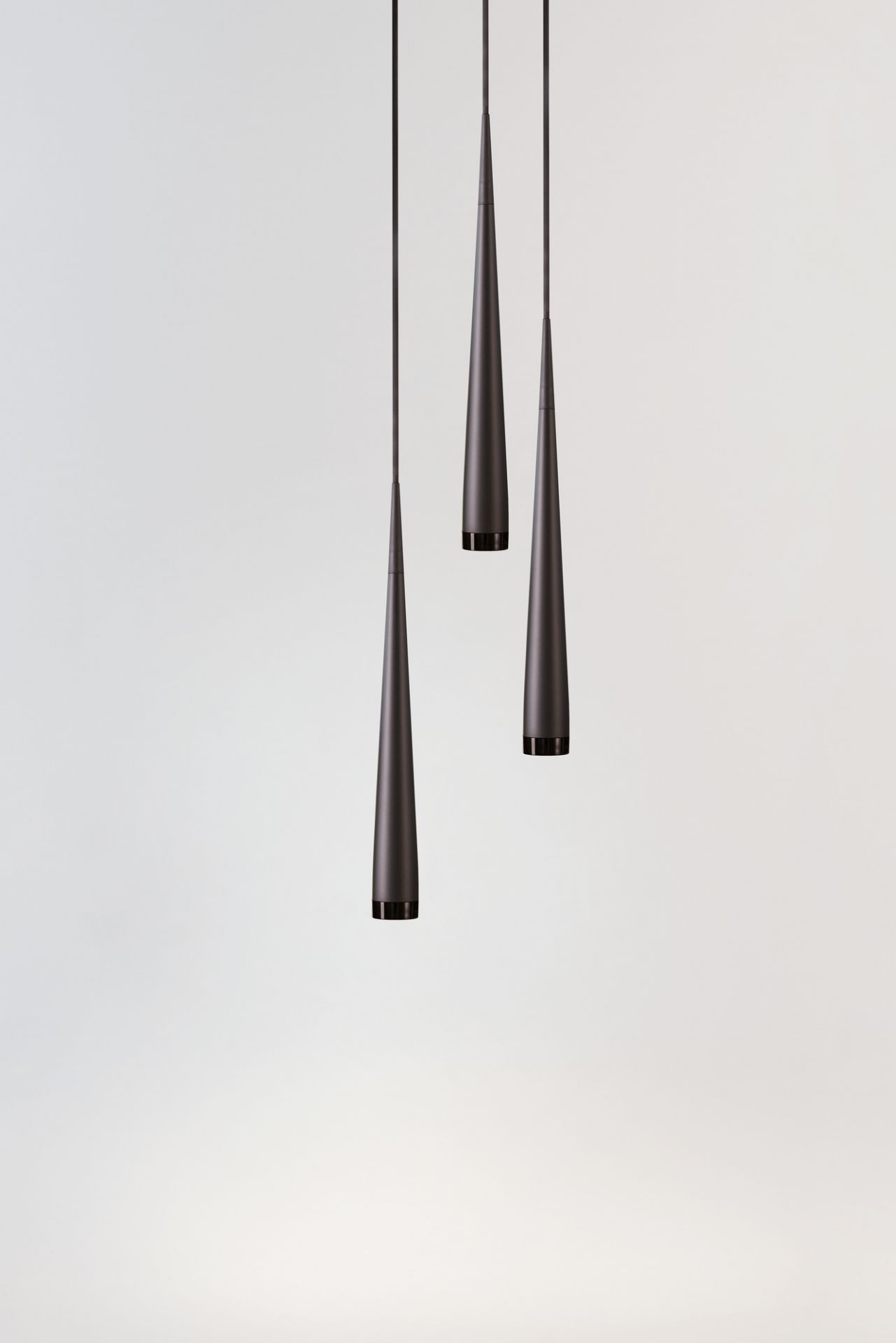 Drei graue, kegelförmige Pendelleuchten von Niceone hängen vor einem hellen Hintergrund.