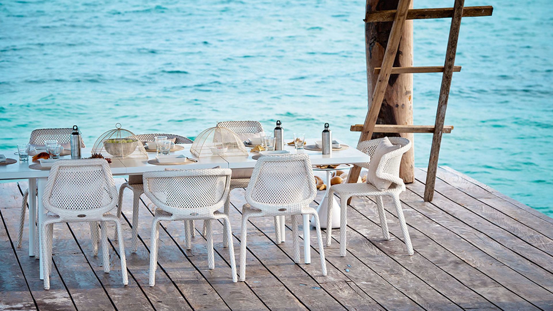 Seashell Armchair von Dedon in Chalk Weiß am Esstisch im Freien mit Meerblick.