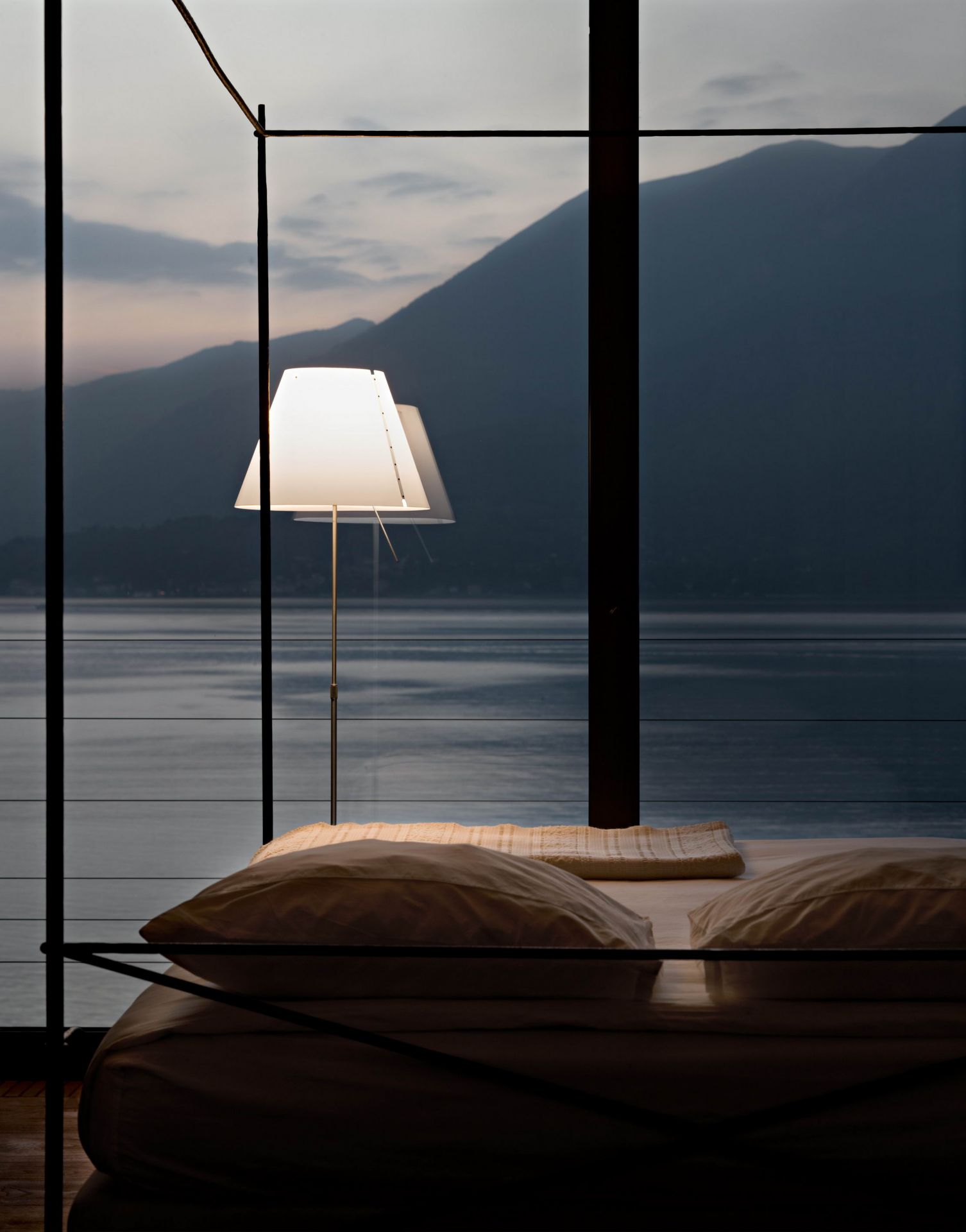 Grande Costanza Stehleuchte von Luceplan neben einem Bett mit Seeblick. Design Lampe.