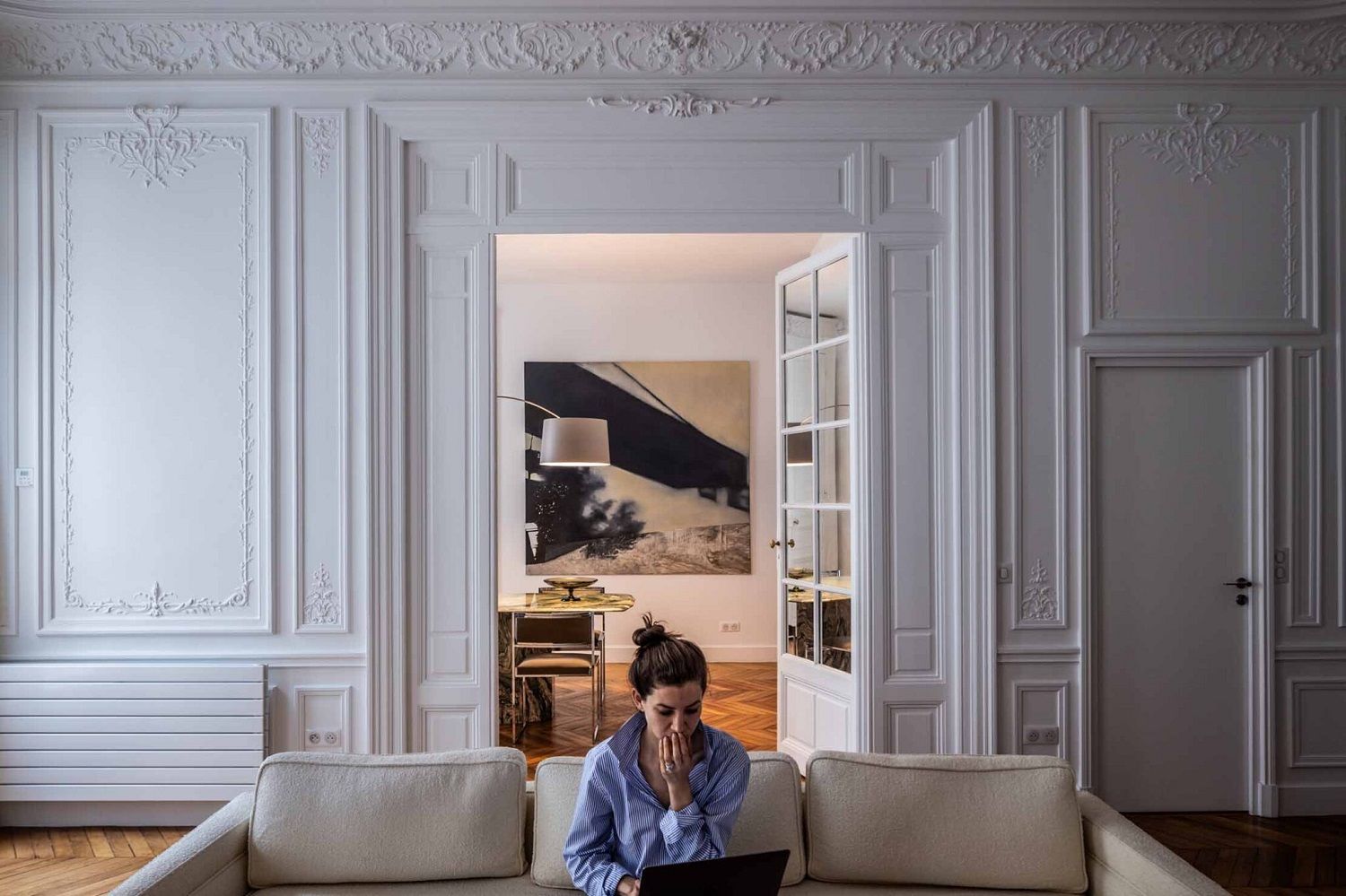 Eine Frau sitzt auf einem Sofa, im Hintergrund die Twiggy Bogenleuchte von Foscarini.