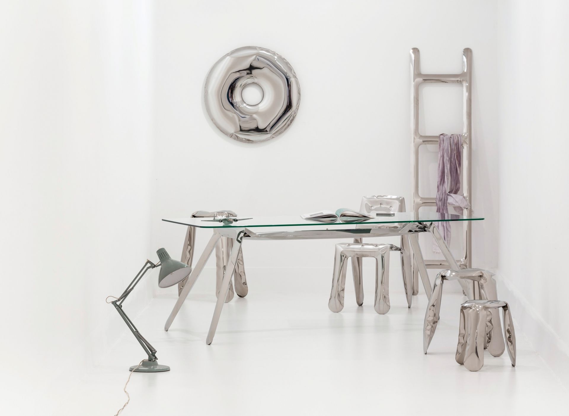 Silberner Rondo Spiegel von Zieta über einem minimalistischen Schreibtisch mit Stühlen und Lampe.