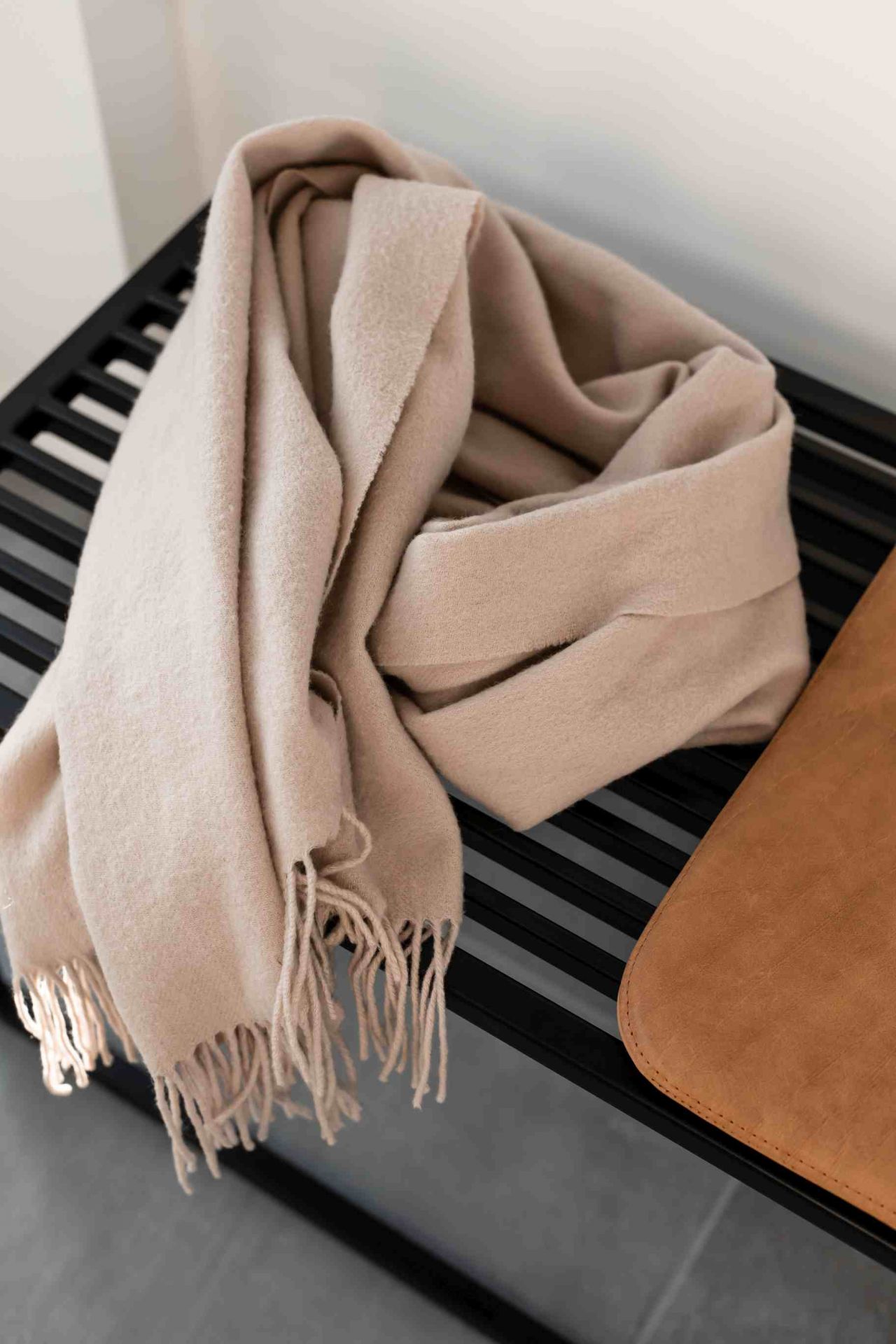 Element Bench Bank: Detailaufnahme einer schwarzen Bank mit beigem Schal und brauner Tasche.