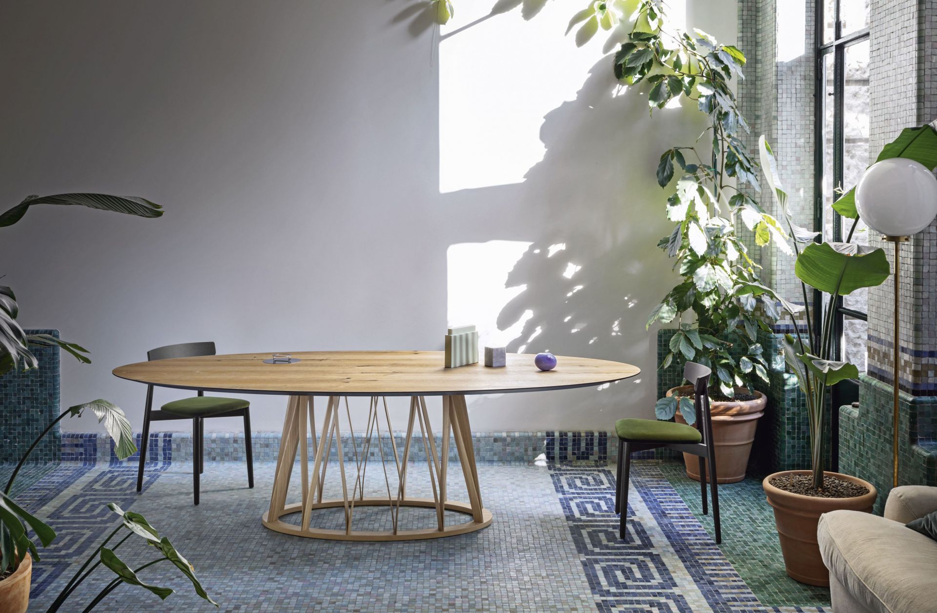 Acco Tisch Miniforms: Ovaler Holztisch mit filigranem Holzgestell in einem hellen, begrünten Raum.