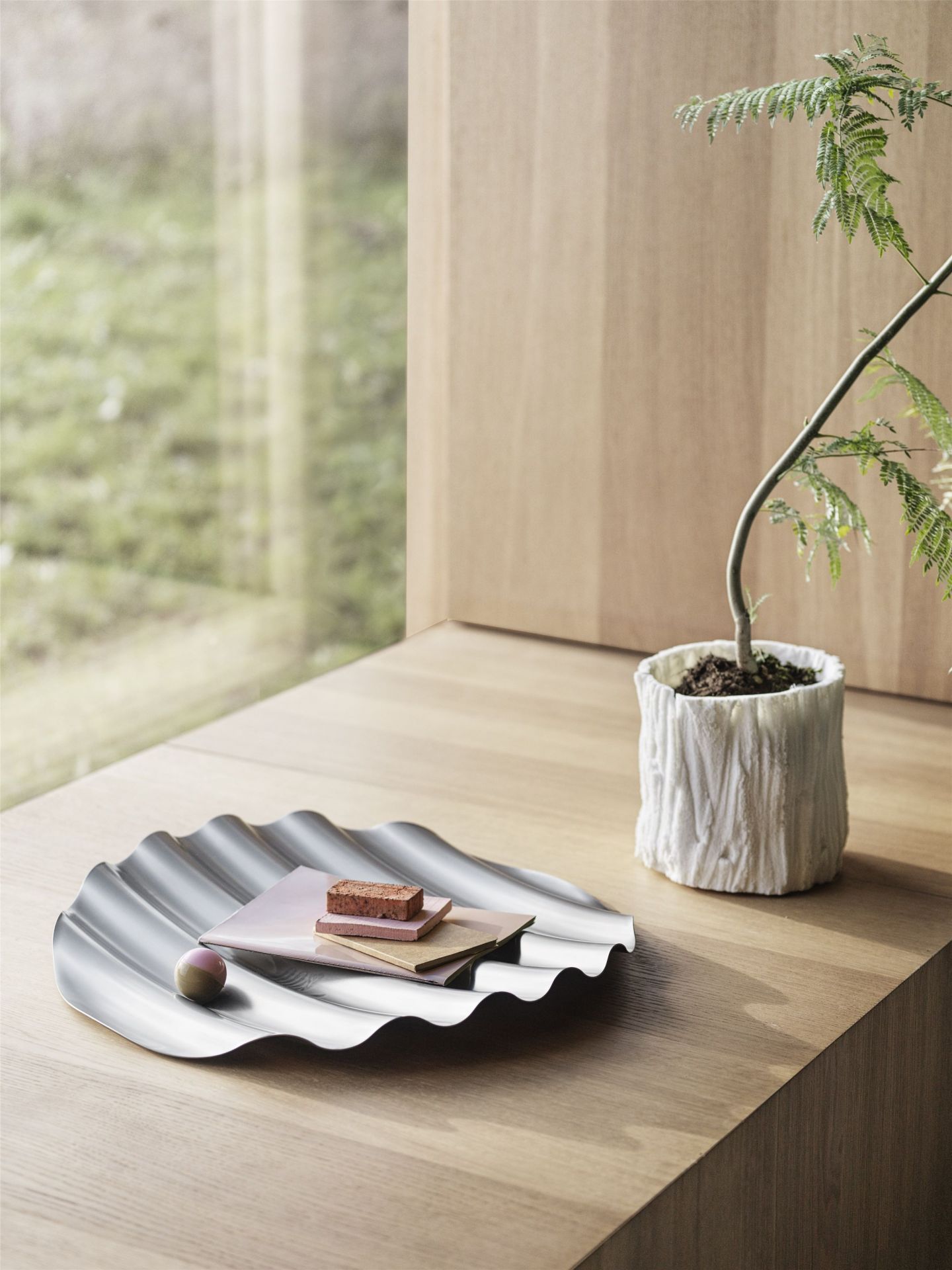 Muuto Wave Tray Schale aus Edelstahl auf Holztisch mit Dekoration und Zimmerpflanze.
