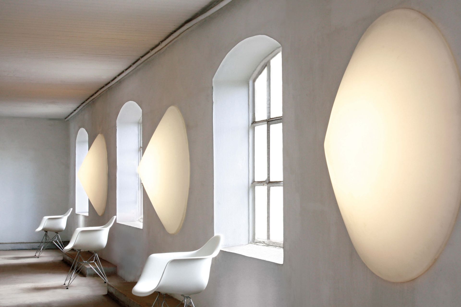 Cao Mao Wandleuchte WL120 LED 4000K Next an einer weißen Wand mit Fenstern und Stühlen.