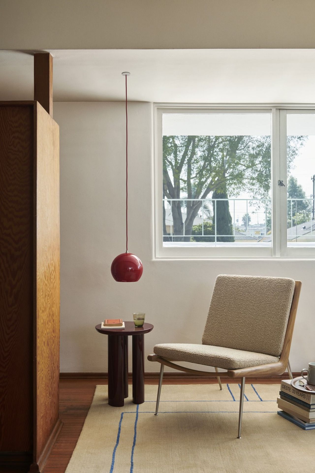 Wohnzimmer mit AndTradition Cruise Teppich, Design-Sessel, roter Pendelleuchte und Beistelltisch am Fenster.