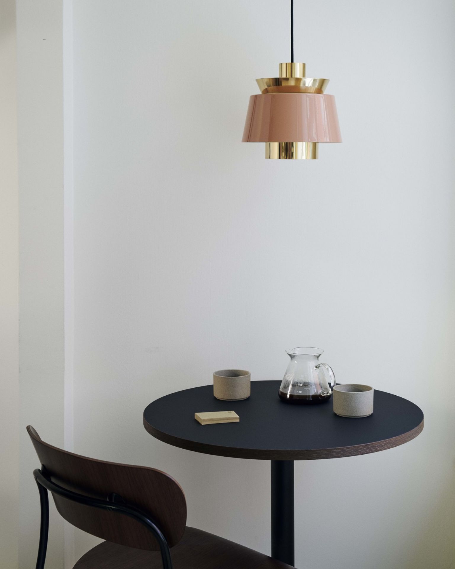 AndTradition Utzon JU1 Pendelleuchte in Rosa und Gold über einem Kaffeetisch mit Karaffe und Tassen.