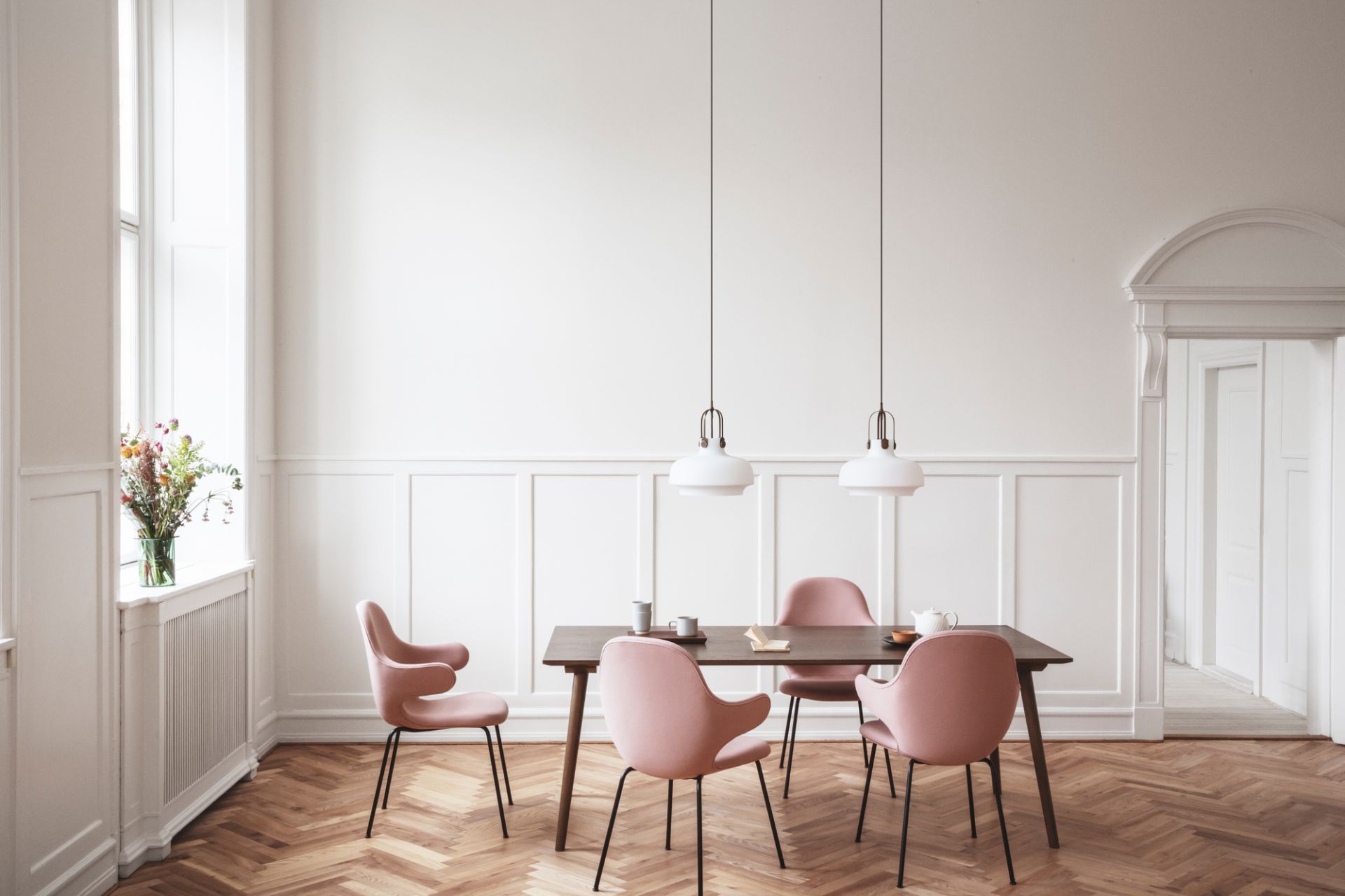 Esszimmer mit Copenhagen Pendelleuchten von AndTradition über einem dunklen Holztisch mit rosa Stühlen.