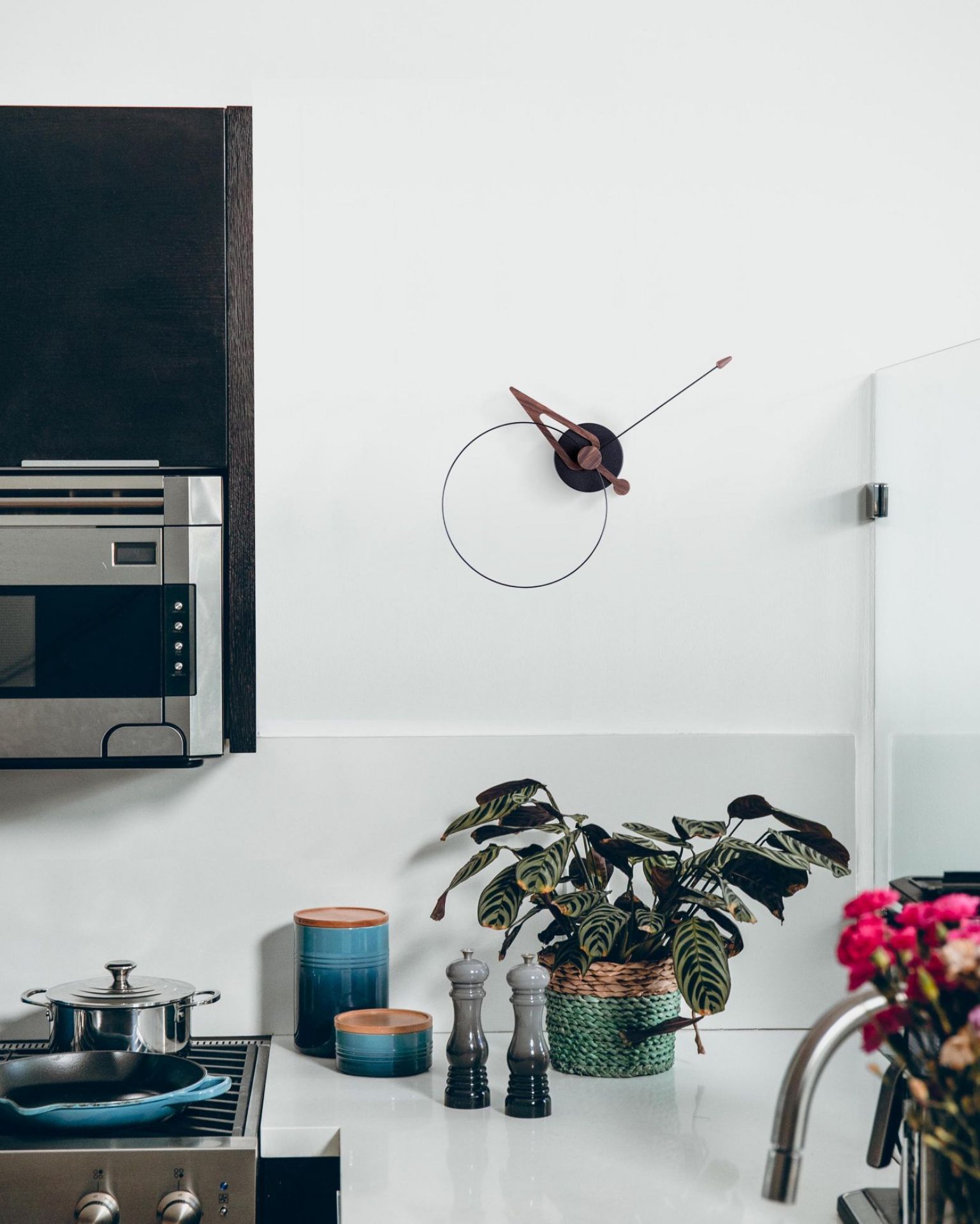 Pico Wanduhr von nomon in Walnuss und Schwarz an einer weißen Küchenwand.
