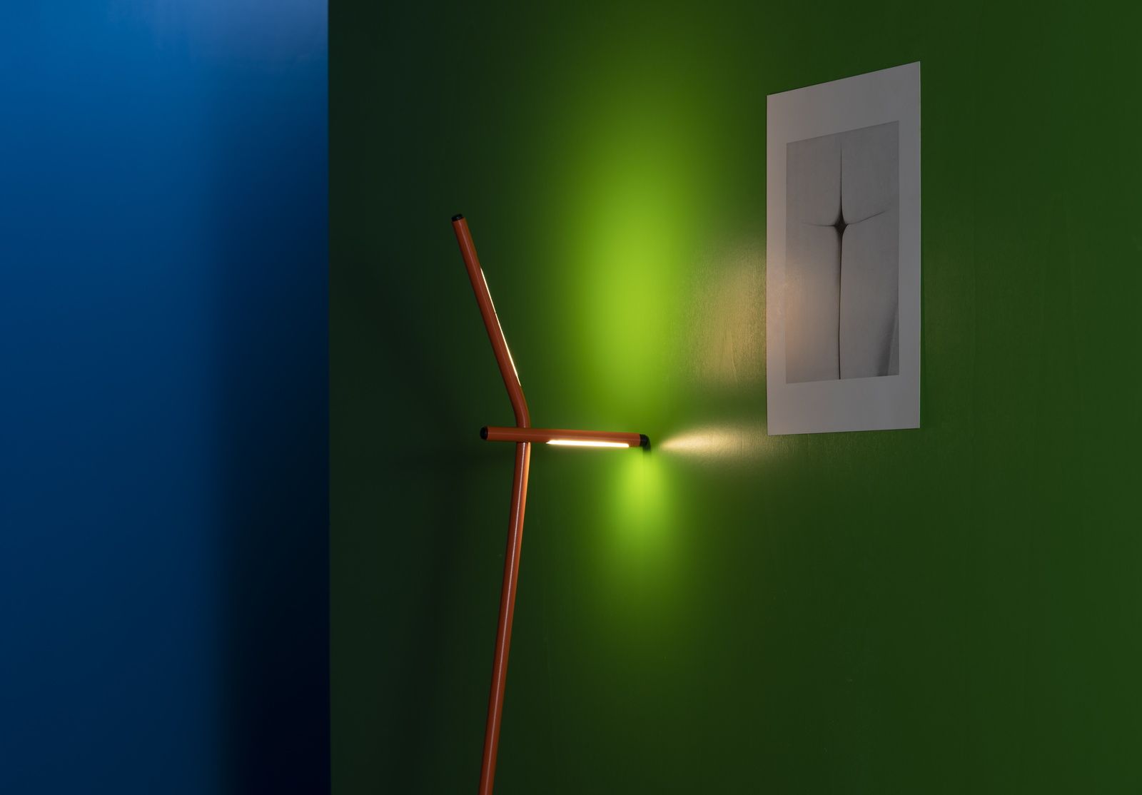 Gru Stehleuchte von Martinelli Luce in Orange vor grüner Wand, modernes Design, Lichtakzent.