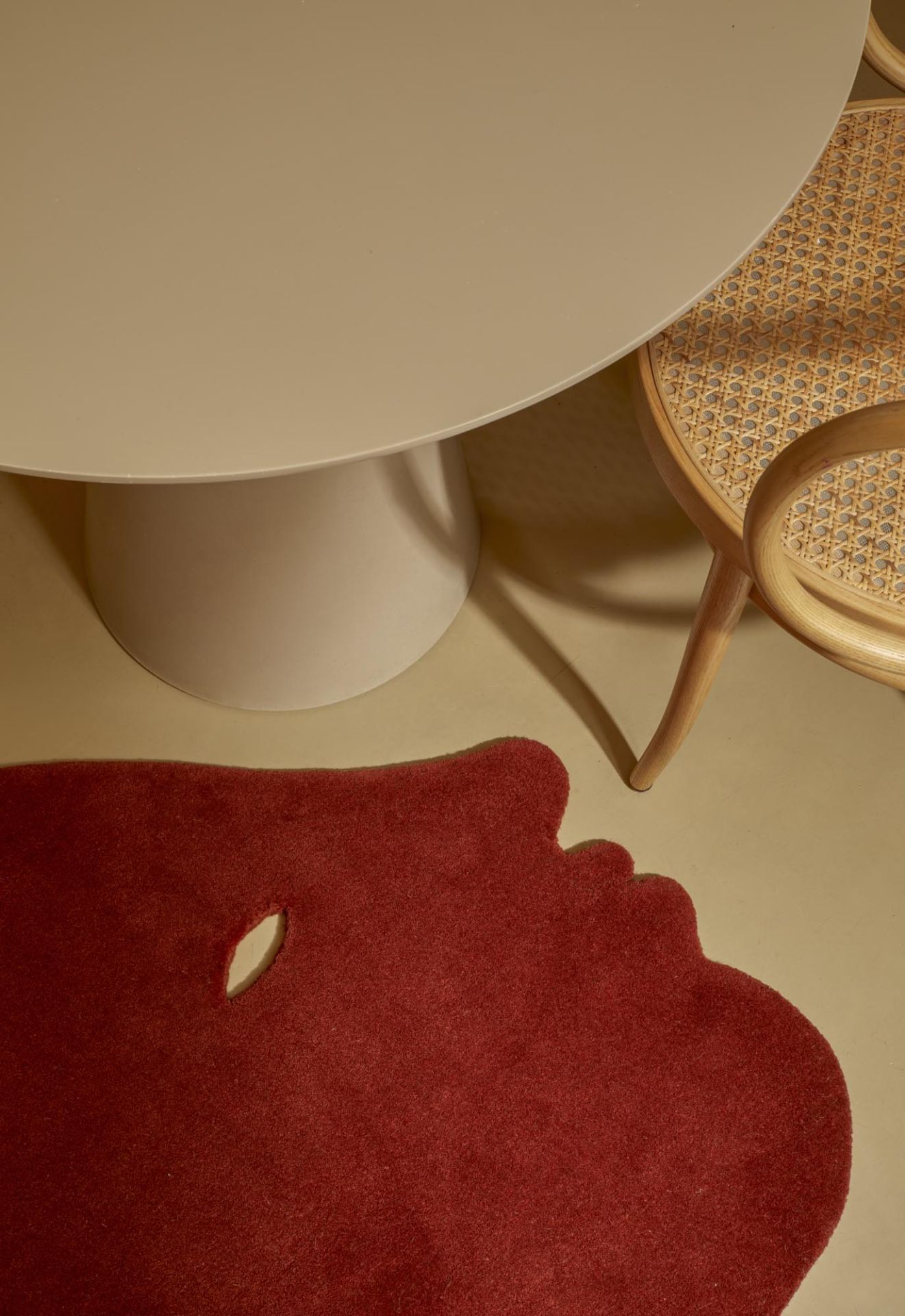 Detailaufnahme des roten Nanimarquina Teppichs "Talk Talk" mit Gesicht-Design unter einem Tisch und Stuhl.