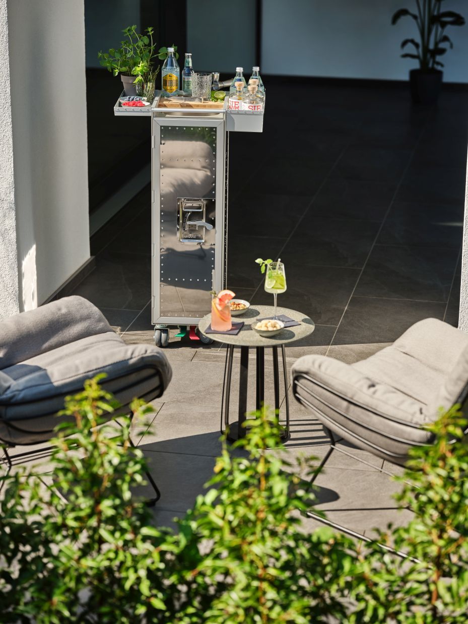 Rivet Rocker Flugzeugtrolley Bordbar mit Getränken und Cocktails auf Terrasse mit Sesseln.